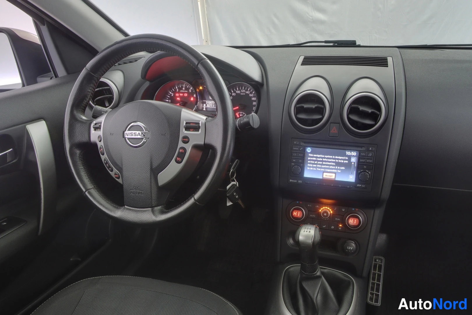 Muu: Ohjaamosta näkyy Nissan-ohjauspyörä, mittaristo ja keskikonsoli, jossa on radio/navigointilaitteet ja manuaalivaihteen vaihdekeppi.