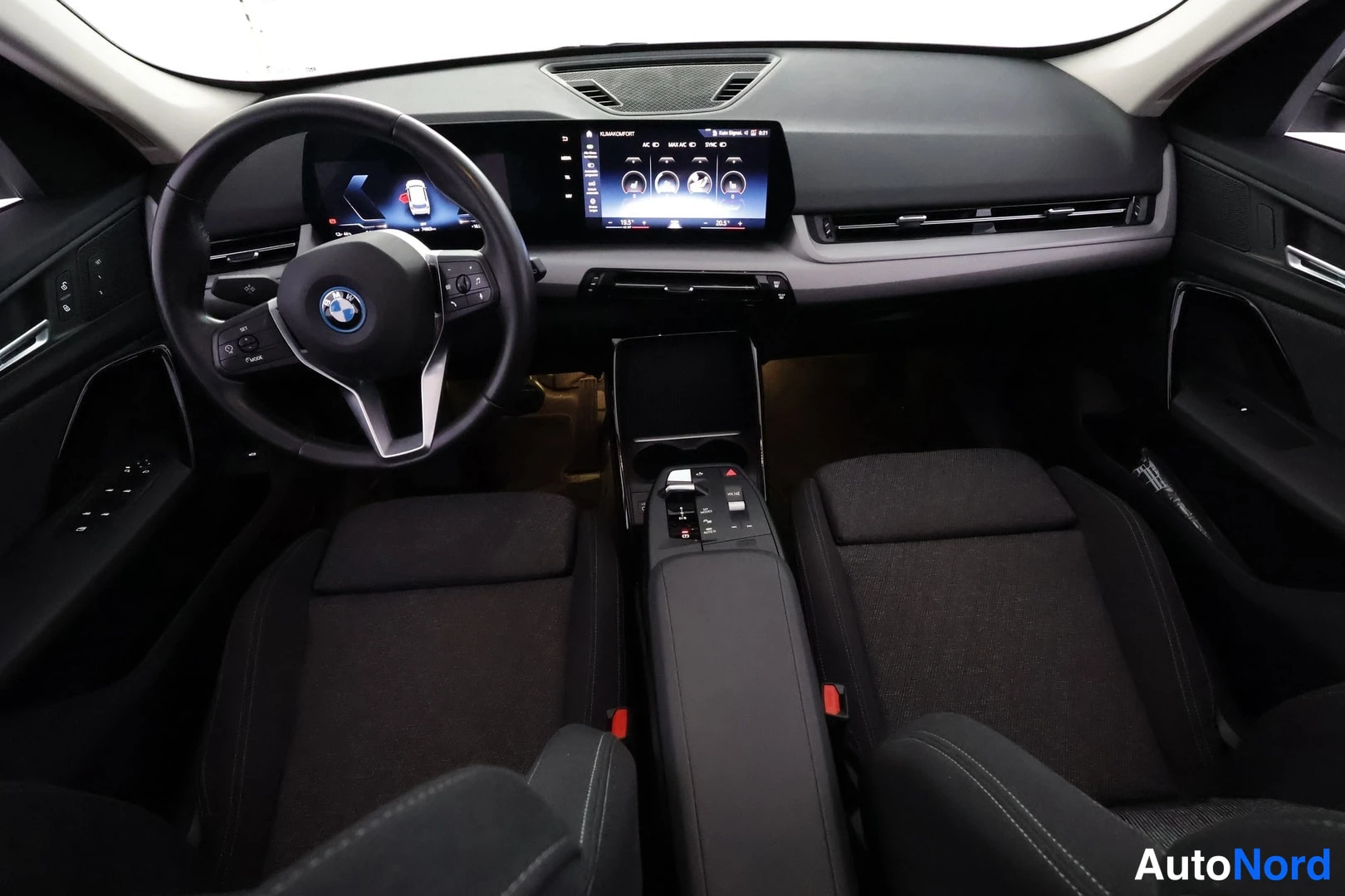 Muu: Kojetaulu ylhäältä kuvattuna: BMW-merkkinen ohjauspyörä, leveä kaareva näyttö, automaattivaihteen valitsin ja keskikonsolin säätimet näkyvissä.