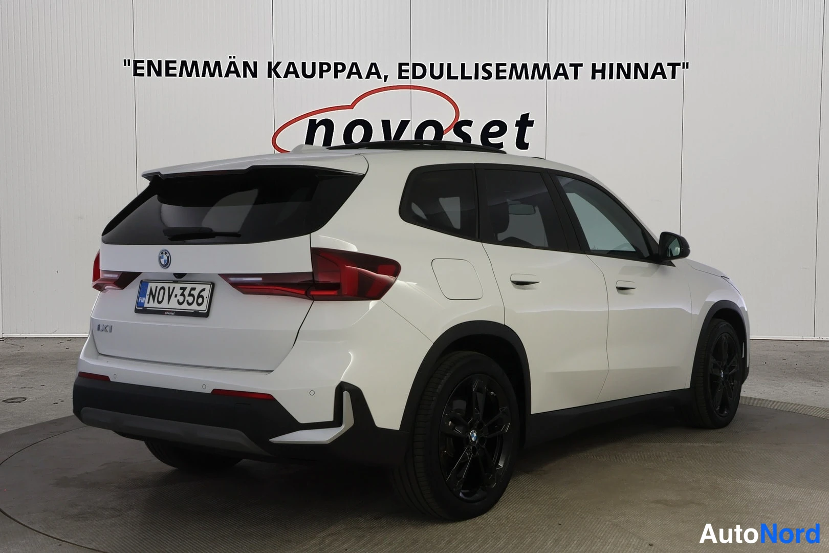 Takaviisto: Valkoinen BMW iX1 takakolmasosanäkymä toiselta sivulta, kattokaiteet näkyvissä, rekisteritunnus.