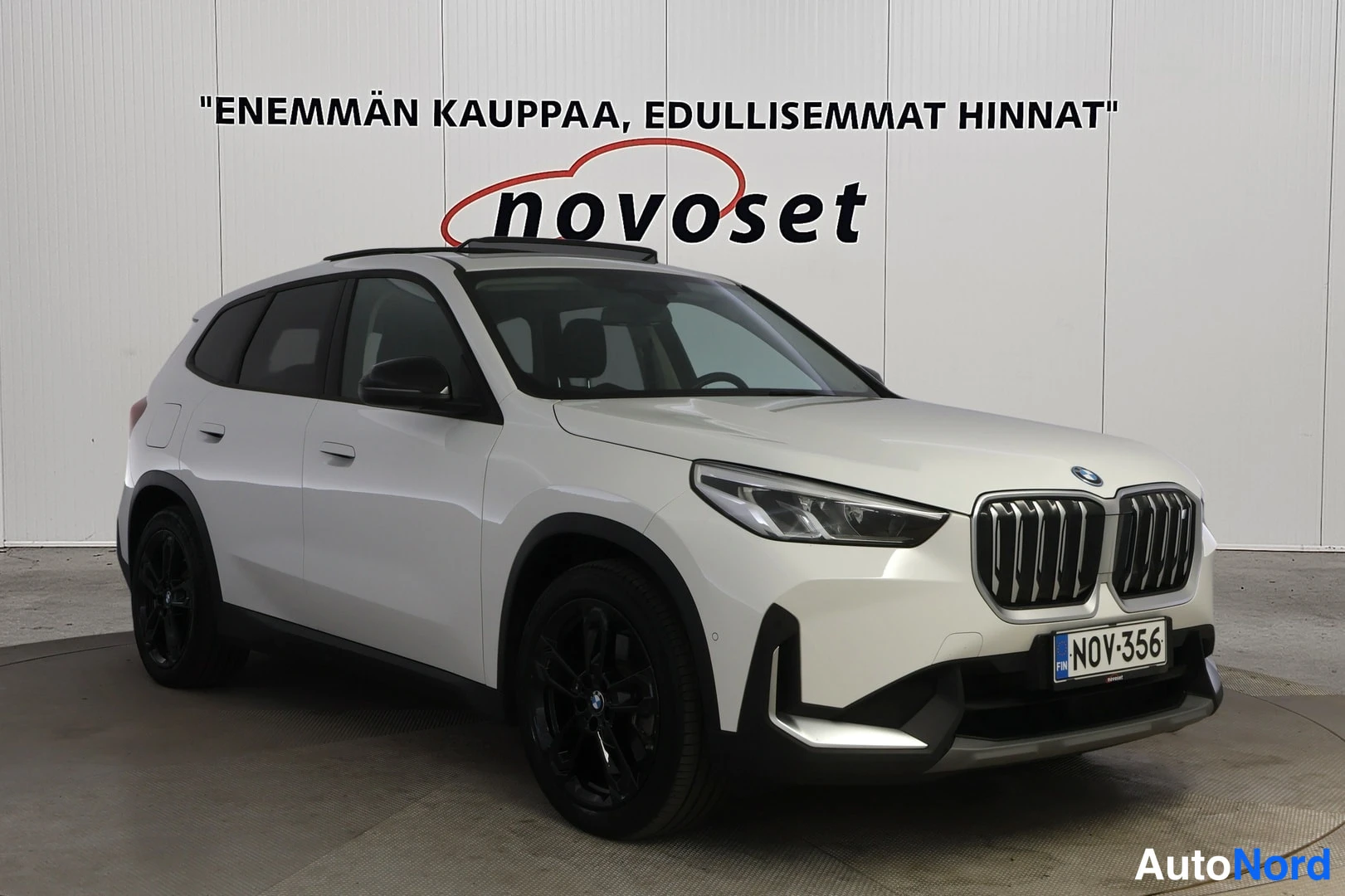 Etuviisto, nokka vasemmalle: Etuviistokuva valkoisesta BMW-katteisesta katto-raideilla varustetusta autoista. Musta puskuri ja pyörät ovat näkyvissä.