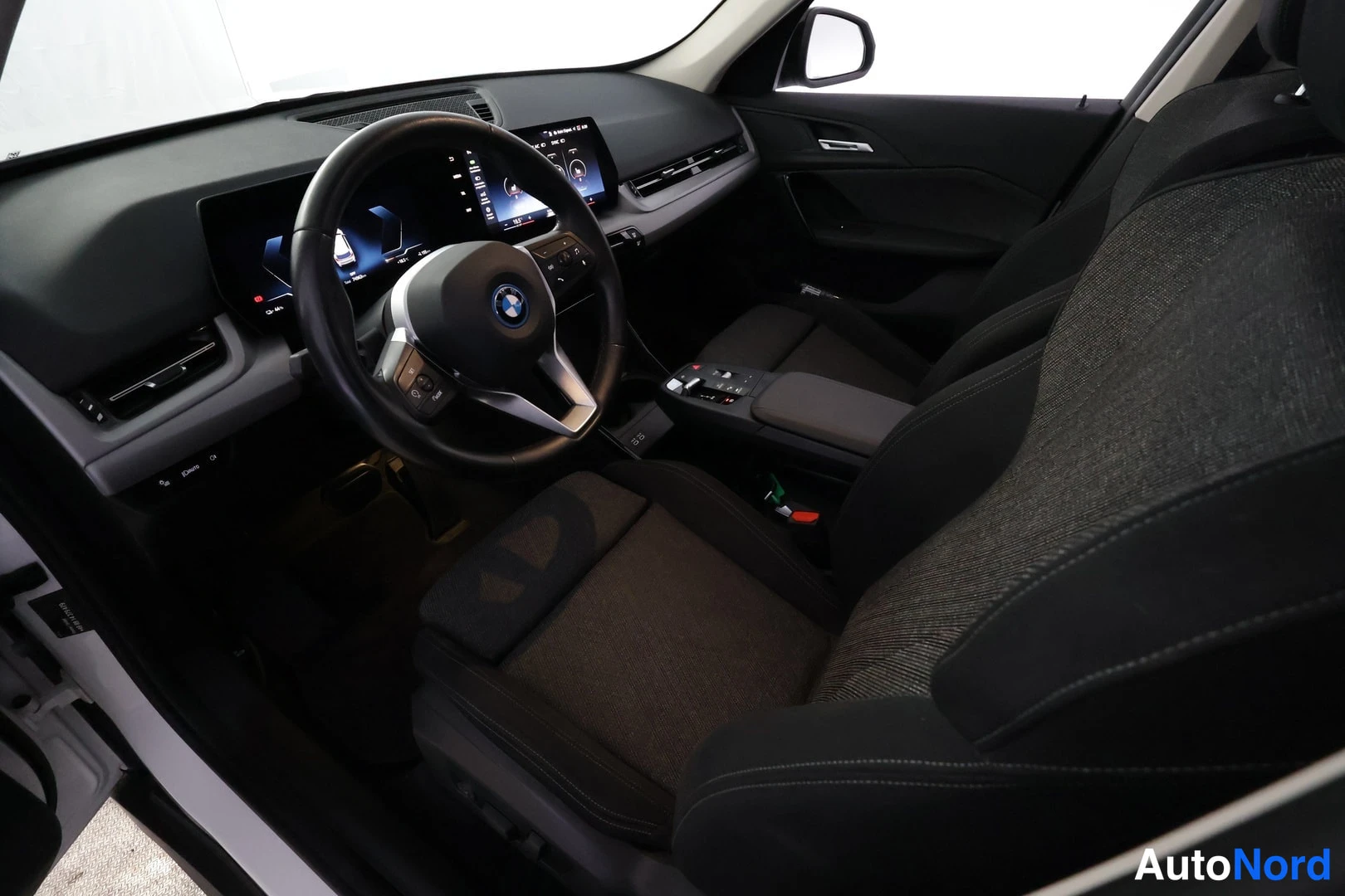 Etuviisto, nokka oikealle: Ohjaamo kuljettajan oven puolelta: BMW-merkillinen ohjauspyörä, kaareva näyttö ja tummat kangasistuimet.