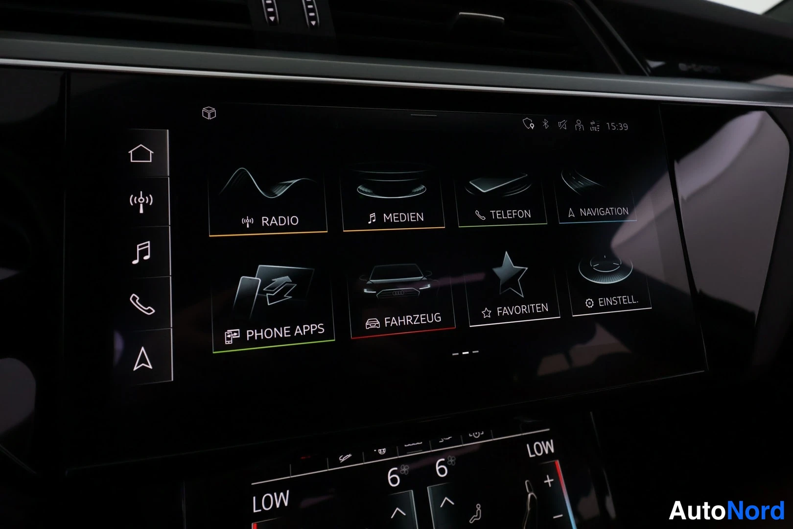 Yksityiskohta: Infotainment-näyttö, jossa RADIO-, MEDIEN-, TELEFON-, NAVIGATION-, PHONE APPS-, FAHRZEUG-, FAVORITEN- ja EINSTELL.-valikot sekä kellosäätimet.