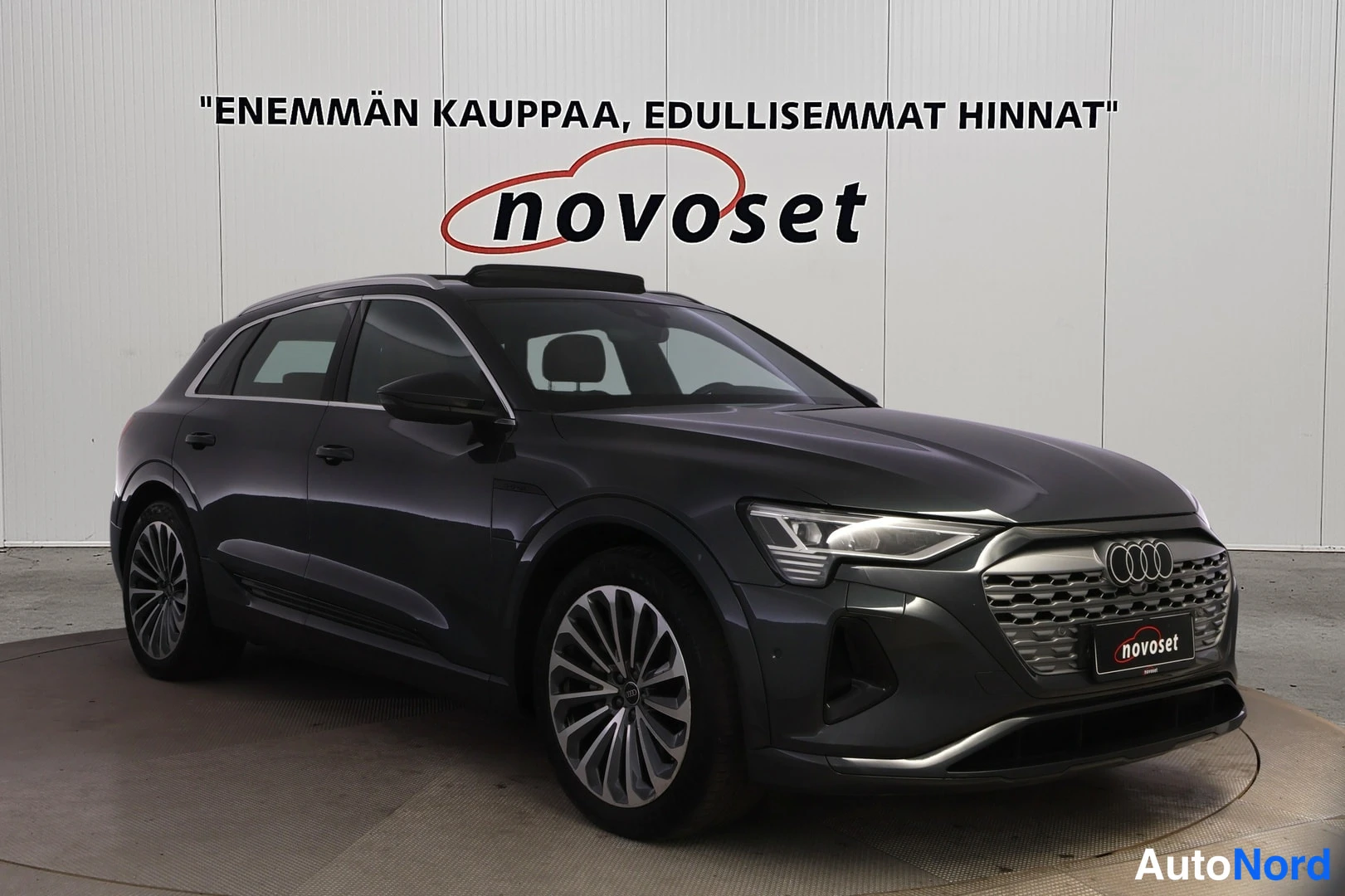 Etuviisto, nokka vasemmalle: Kuvan vasemmassa etulaidassa on tummansininen Audi, jossa näkyvät etuosa ja auton oikea puoli. Kuvassa on myös takakatto.