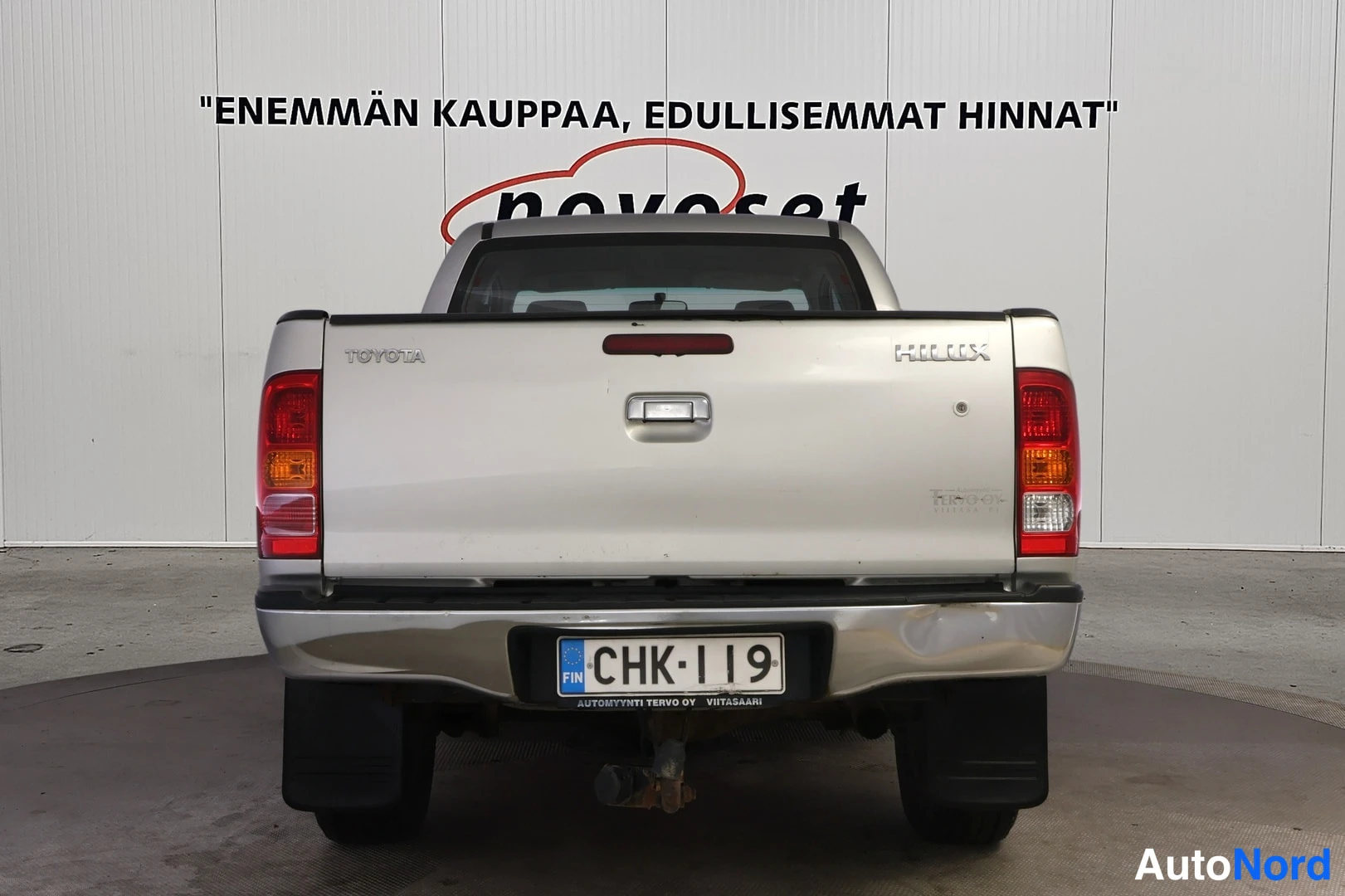 Takaa: Hopeanvärinen Toyota Hilux suoraan takaa kuvattuna; Toyota- ja Hilux-tunnukset, takavalot sekä rekisterilauta näkyvät.