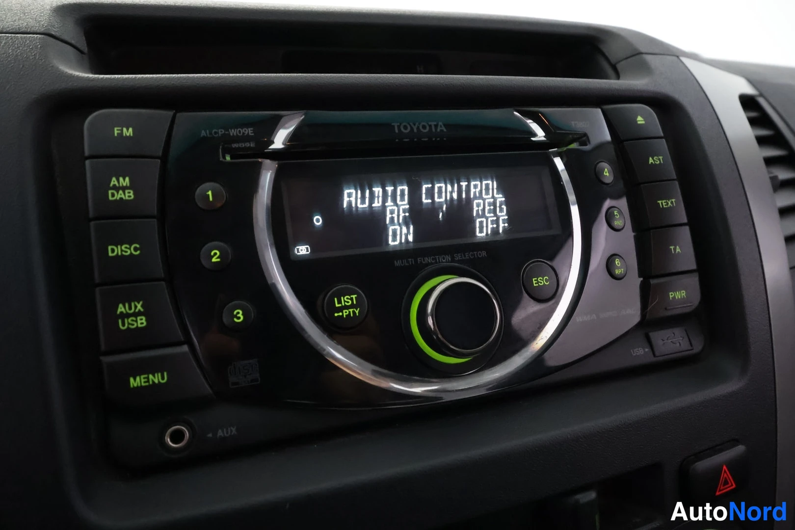 Muu: Toyota-merkkisen radion näyttö tekstillä 'AUDIO CONTROL RF: REG ON / OFF', ympärillä painikkeet FM, AM/DAB, DISC, AUX/USB, MENU, AST, TEXT, TA, PWR.