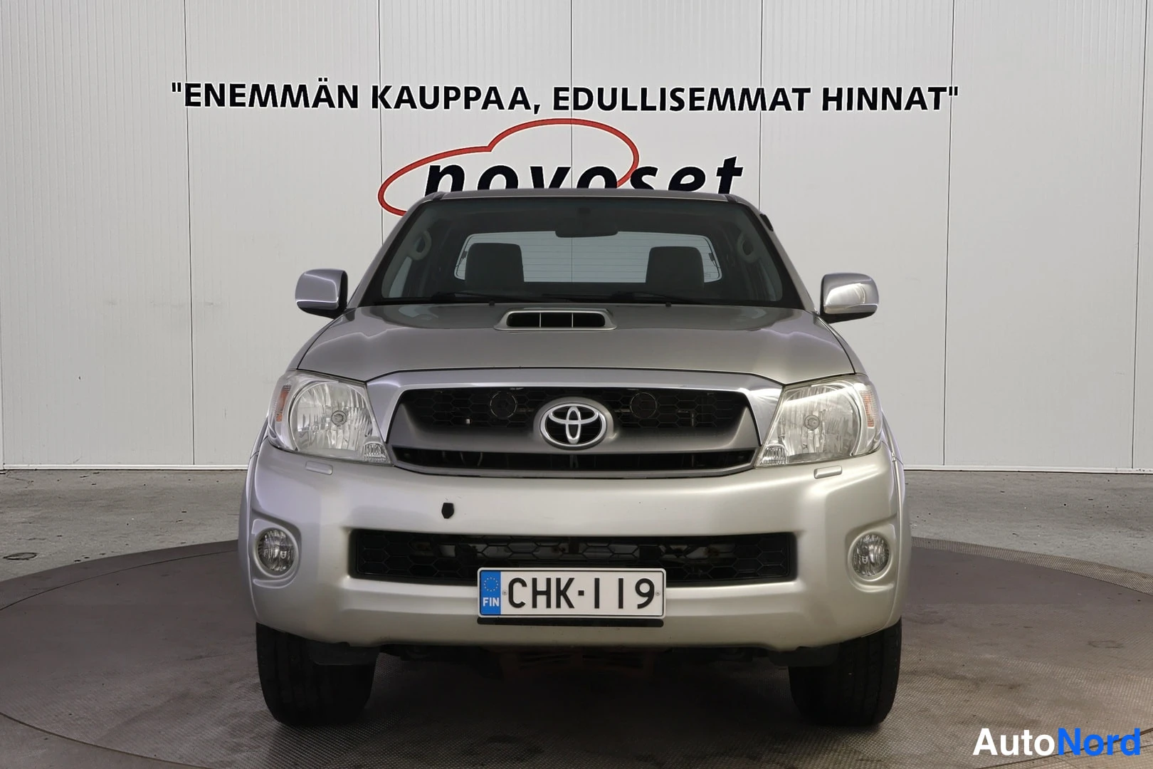 Edestä: Hopeanharmaa Toyota Hilux -auto suoraan edestä päin kuvattuna, rekisterikilpi.