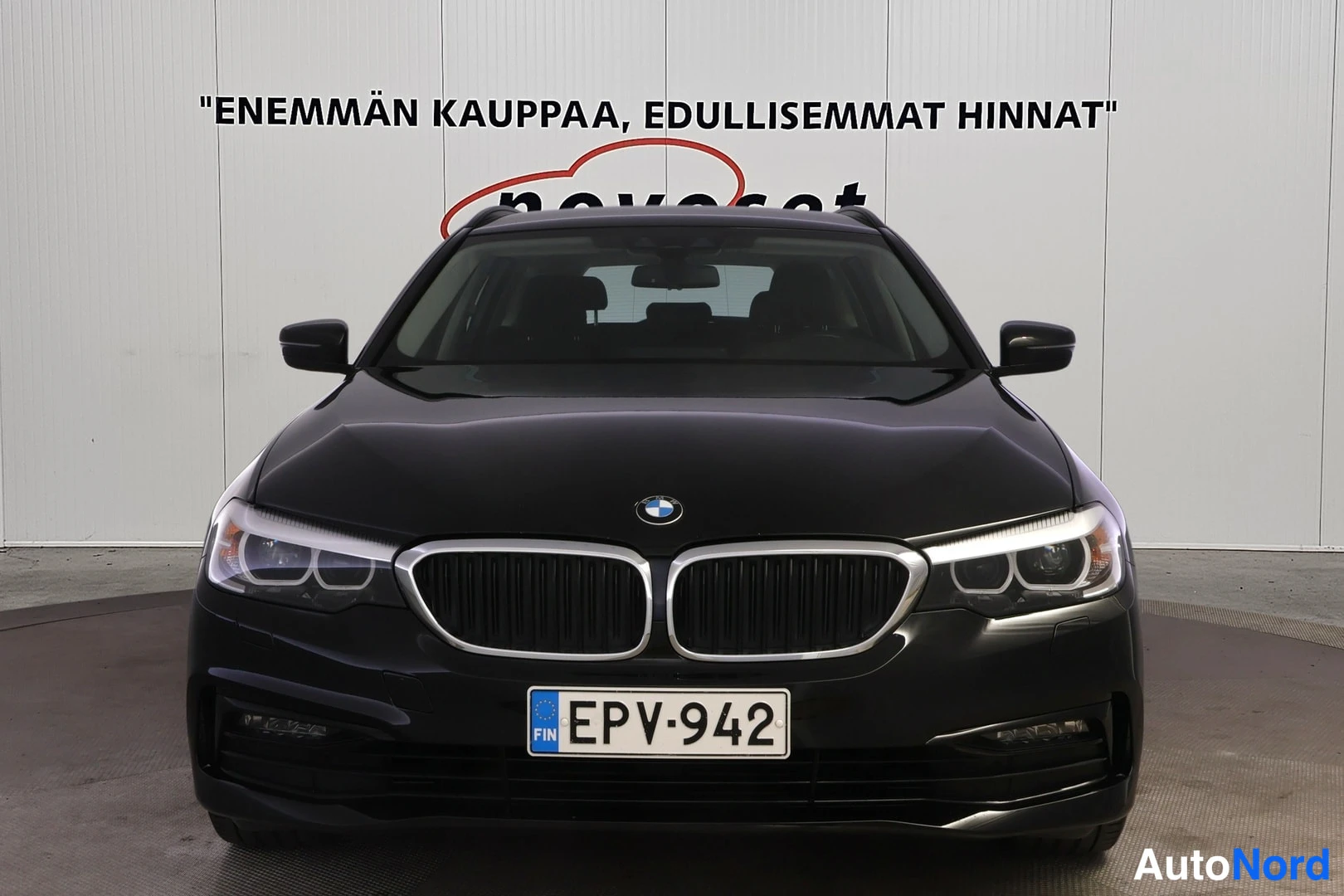 Edestä: Mustan farmariauton suora etukuvakulma, BMW-merkki keulalla, rekisteritunnus, 'FIN' sinisessä EU-tunnisteessa.