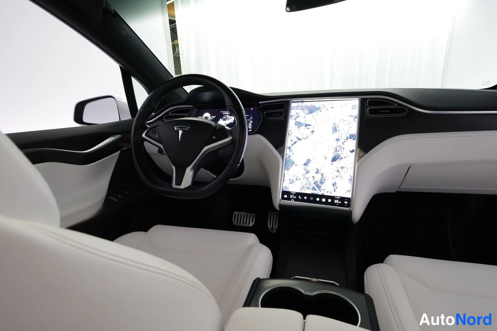 Etuviisto, nokka vasemmalle: Ohjaamo valkoisin nahkapenkein, Tesla-ohjauspyörä ja kartta keskikonsolin näytöllä.