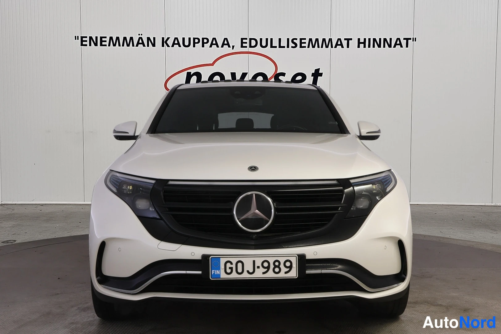Edestä: Kuvassa näkyy etukorkeuden takaa katsottuna valkoinen Mercedes-Benz. Auton etuosassa on suuri merkki ja rekisterikilpi.
