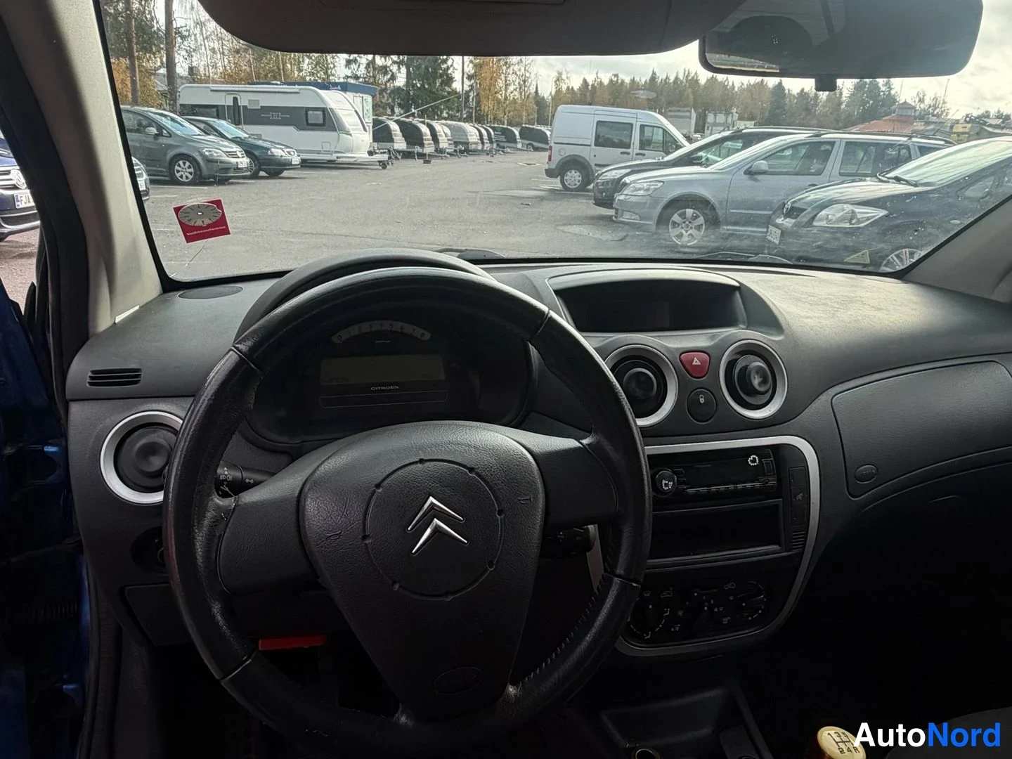 Etuviisto, nokka vasemmalle: Kojelauta ja ohjauspyörä lähikuvassa: Citroën-tunnus ohjauspyörässä, mittaristo, pyöreät tuuletusaukot sekä keskikonsolin soitin ja säätimet.