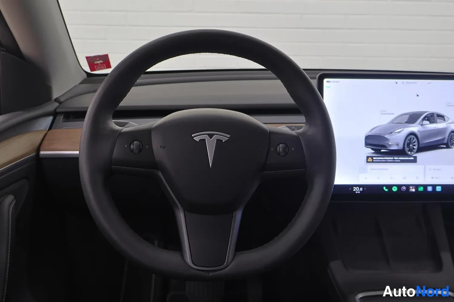 Muu: Lähikuva ohjauspyörästä, keskellä Tesla-logoomeri, kosketusnäyttö osittain näkyvällä oikealla.