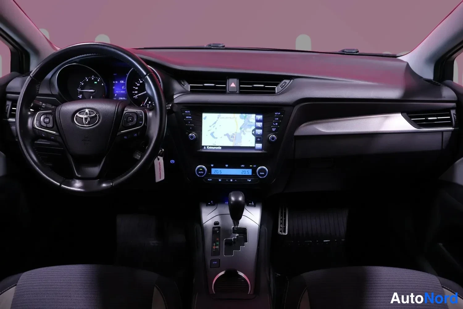 Muu: Toyota Avensisin ohjaamo nähtynä eteenpäin: kuljettajan ohjauspyörä Toyota-merkillä, mittaristo, kosketusnäytöllinen radio karttanalussa ja automaattivaihteisto