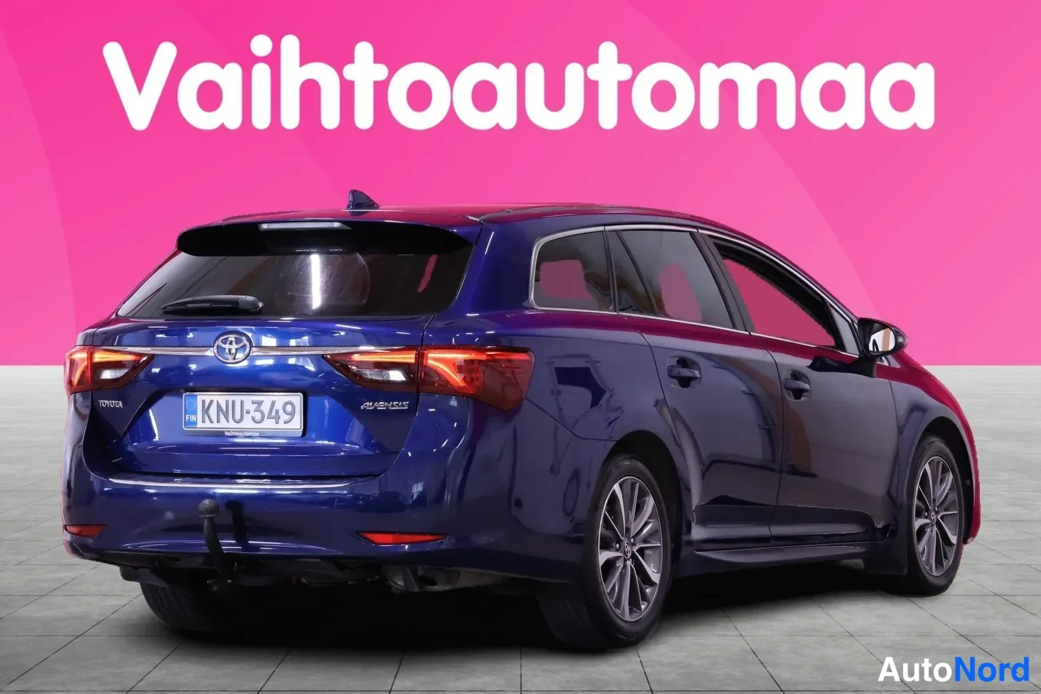 Takaviisto: Sininen Toyota Avensis farmari takaa kulmasta kuvattuna pinkkiauraa studiossa.