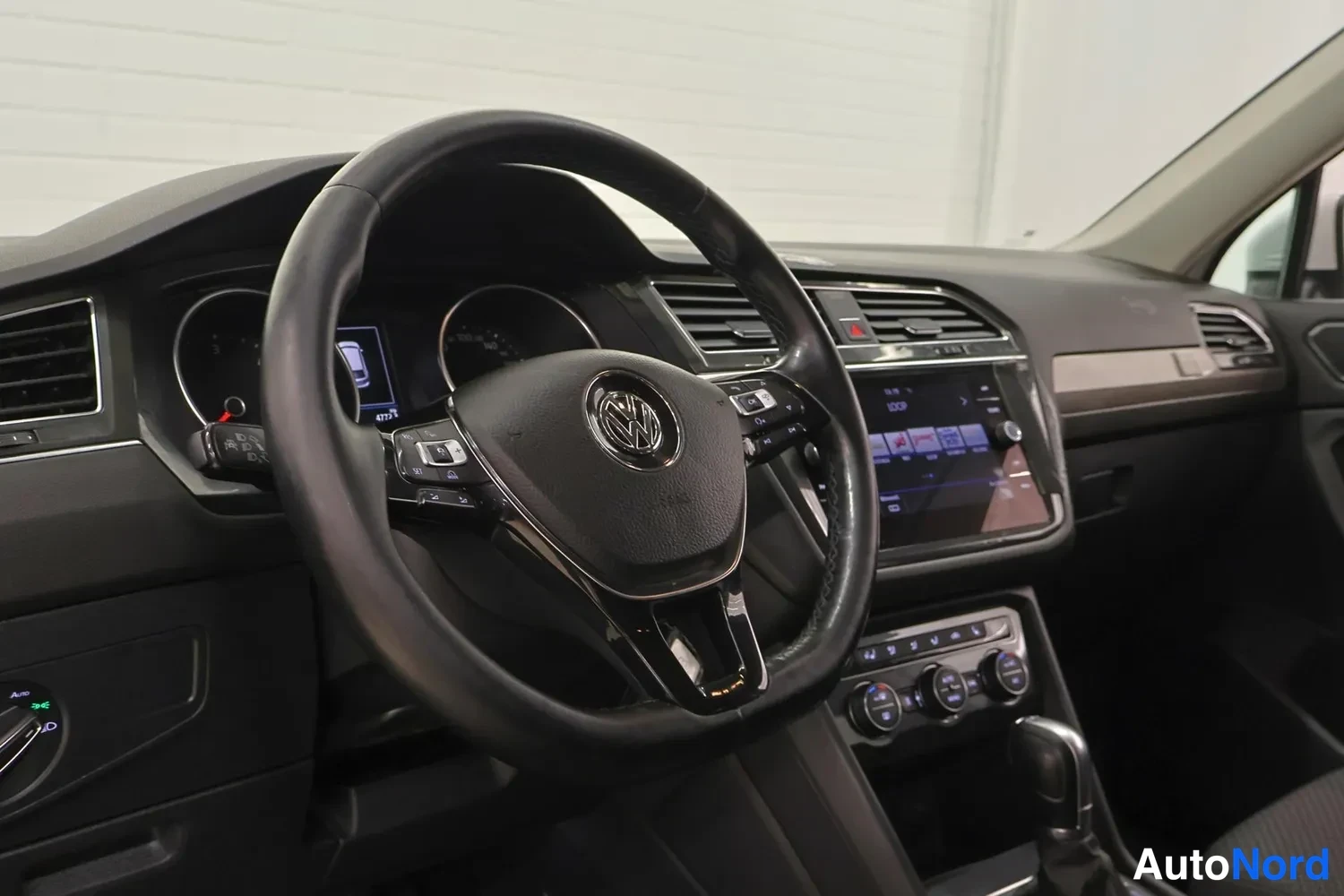 Muu: Ohjaamo lähikuvassa: Volkswagen-merkillä varustettu ohjauspyörä, kosketusnäytöllinen infotainment-järjestelmä ja automaattivaihteiston valitsin.