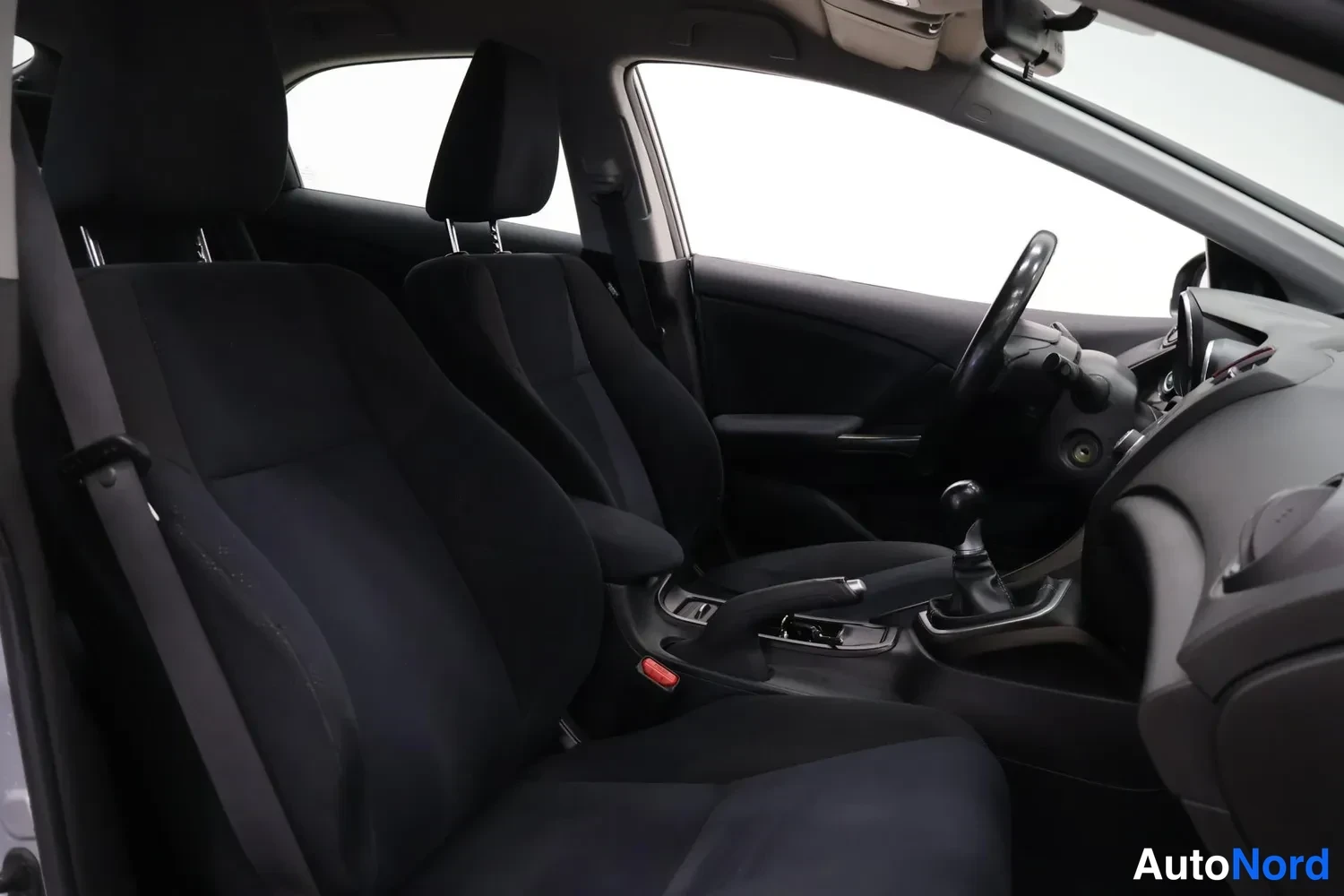 Muu: Honda Civican sisätila: etumatkustajan ja kuljettajan istuimet, ohjauspyörä ja manuaalivaihtohebo tummassa kuosissa.