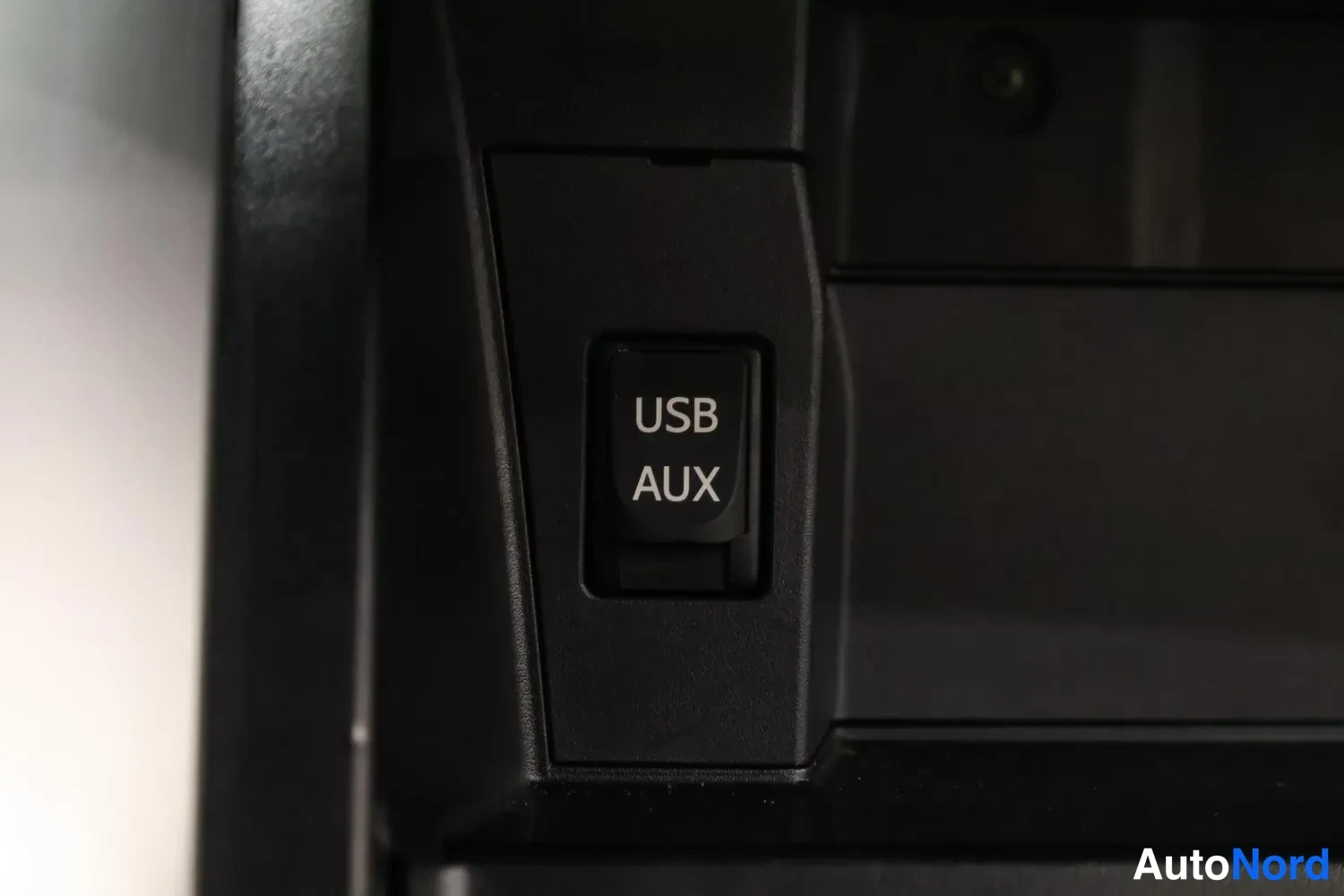 Yksityiskohta: Sisätilakuvan lähikuva keskikonsolin panelista, jossa on merkitty USB- ja AUX-liitännän kansi.