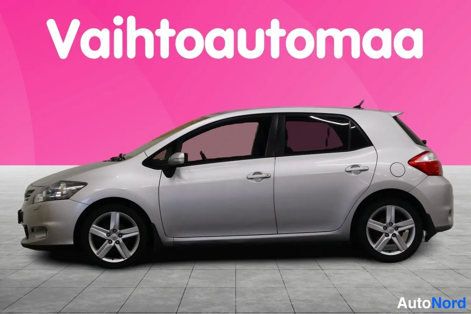 Etuviisto, nokka vasemmalle: Hopeanharmaa Toyota Auris -viistoperä kuvattu edestä vasemmalta, vaaleat piiret ja viisikanta-vanteet näkyvissä.