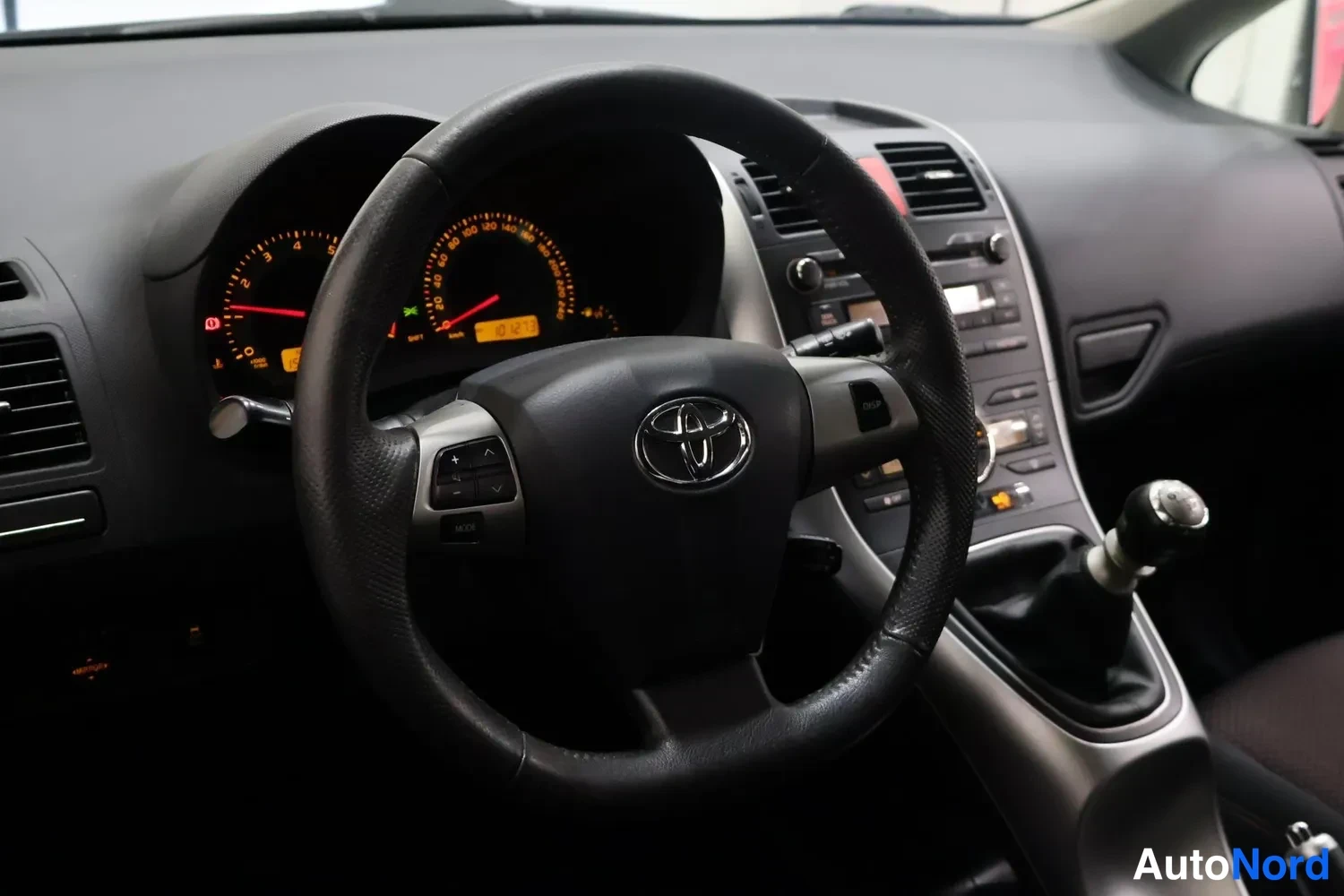 Muu: Ohjaamo näkyy rattipöydältä: Toyota-merkitty ohjauspyörä, mittaristo ja keskitaso.