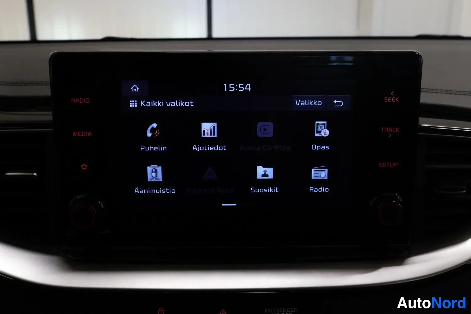 Muu: Istuinseudun infotainment-näyttö, jossa näkyy kaikki valikot: Puhelin, Ajotiedot, Opas, Äänimuistio, Suosikit ja Radio; kelloselvä aikana 15:54.