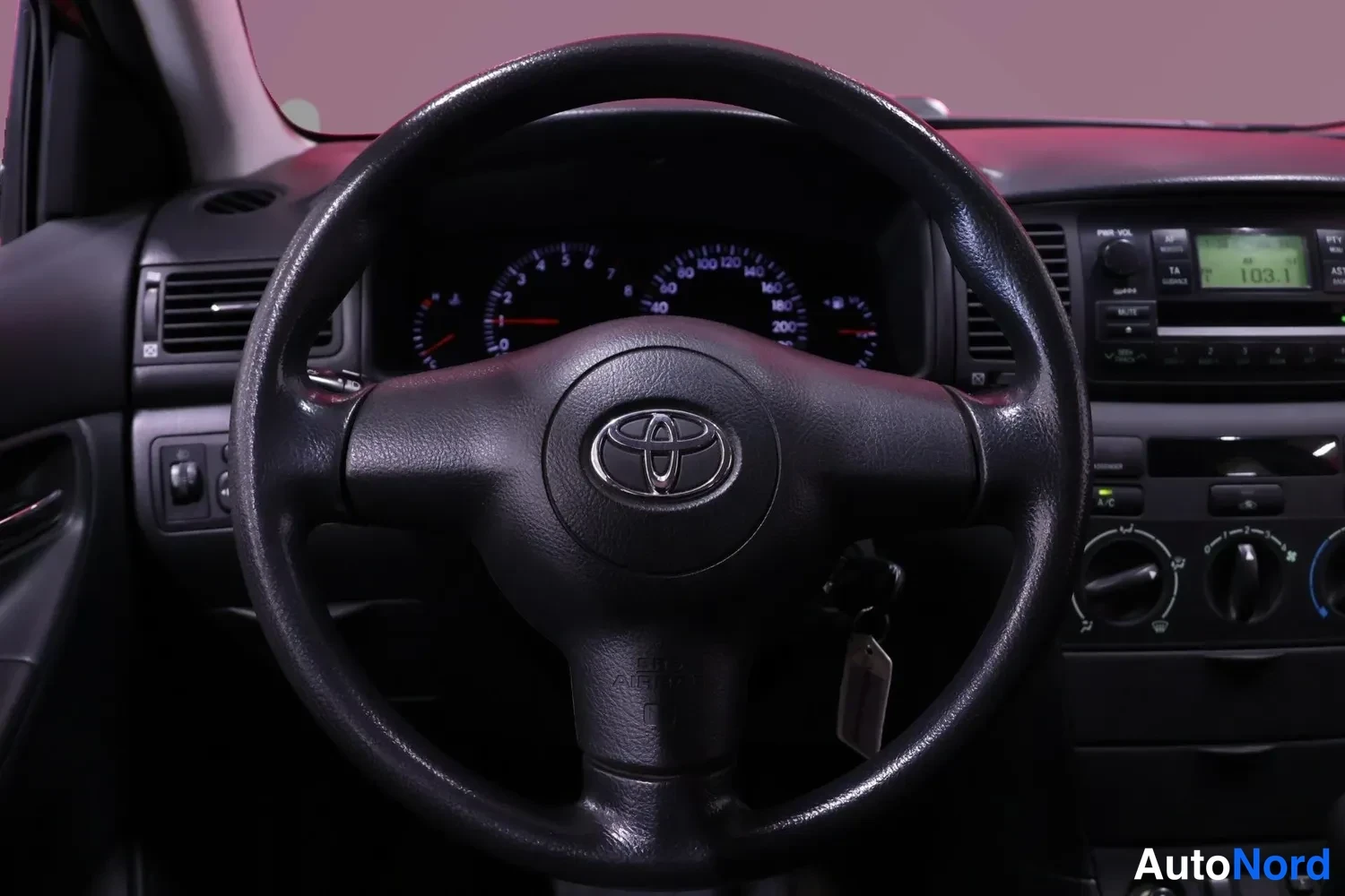 Muu: Lähikuva ohjauspyörästä: Toyota-emblemä ja mittarit näkyvät; avain on kytketty.