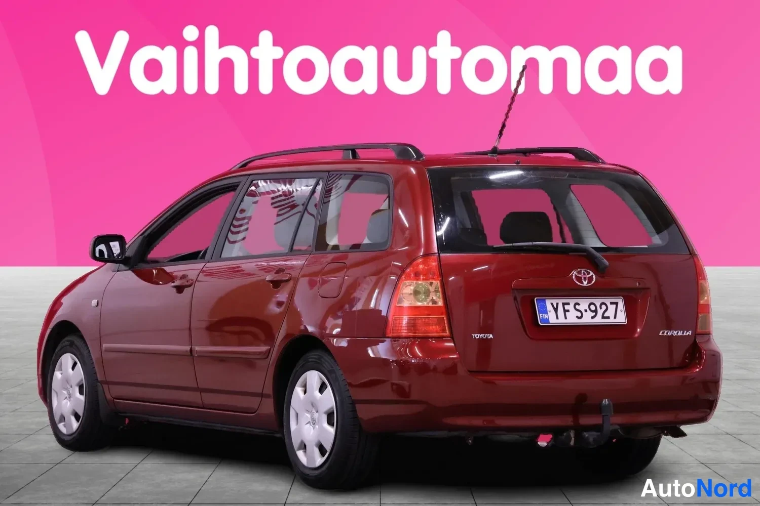 Takaviisto: Punaisen tumma Toyota Corolla -farmari takaviistosta kuvattuna; rekisterikilpi, kattokaiteet ja takana vetokoukku näkyvissä.