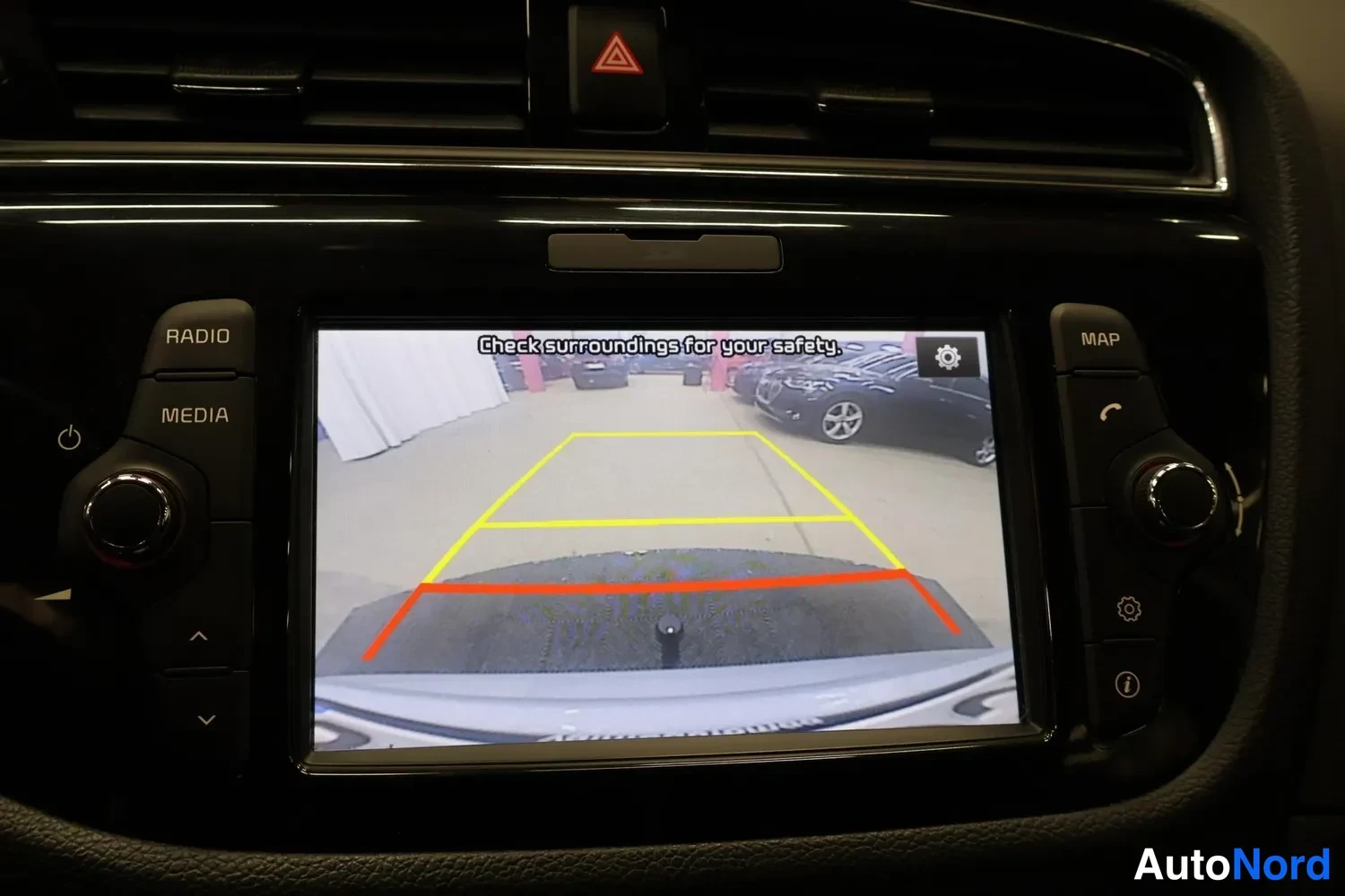 Yksityiskohta: Keskconsole-näyttö näyttää peruutuskameran kuvaa opasteviivoilla ja tekstillä 'Check surroundings for your safety.'