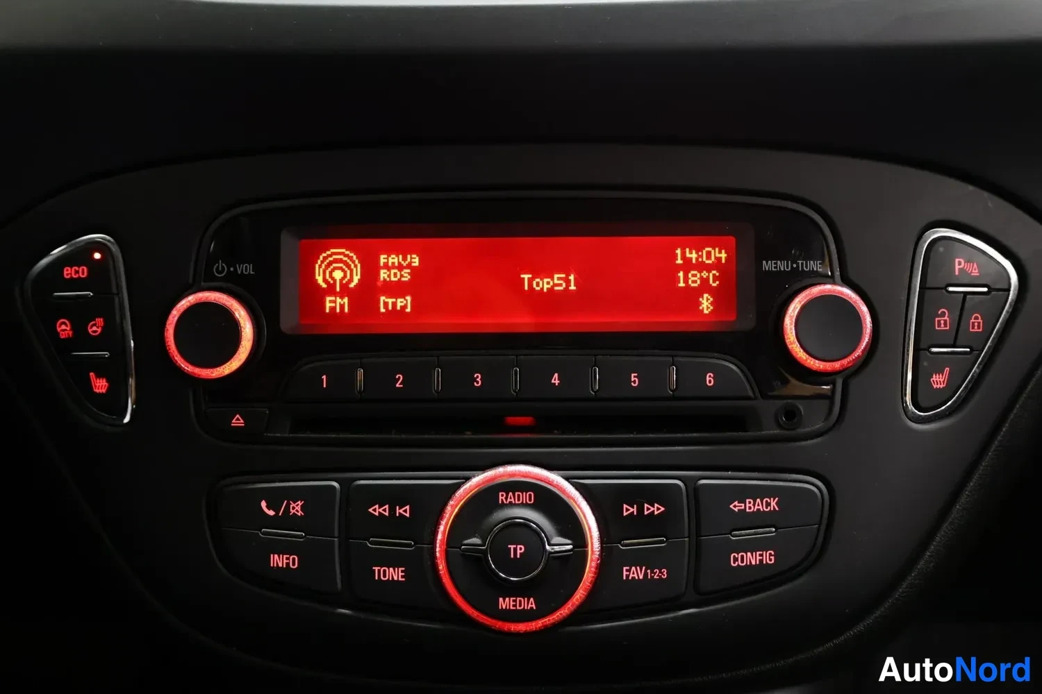 Muu: Merkkipaneeli: punainen näyttö näyttää FM-radioaseman Top51, kellon 14:04 ja lämpötilan 18 °C; painikkeet RADIO, MEDIA, TP ja CONFIG.