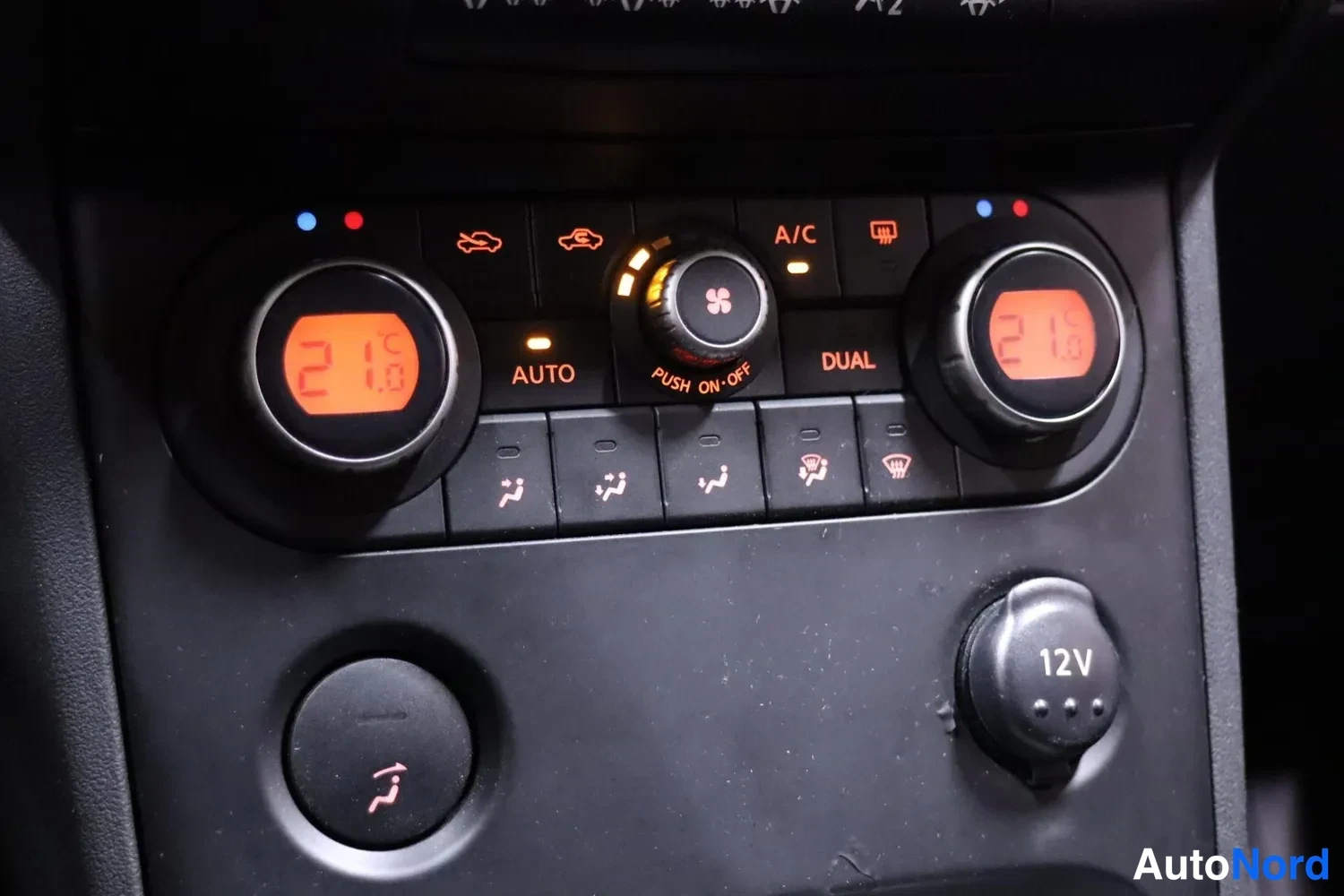 Muu: Ilmastointipaneeli, jossa näyttää molemmin puolin lämpötila 21 astetta, napit AUTO, DUAL, A/C, PUSH ON-OFF ja 12V-pistorasia.