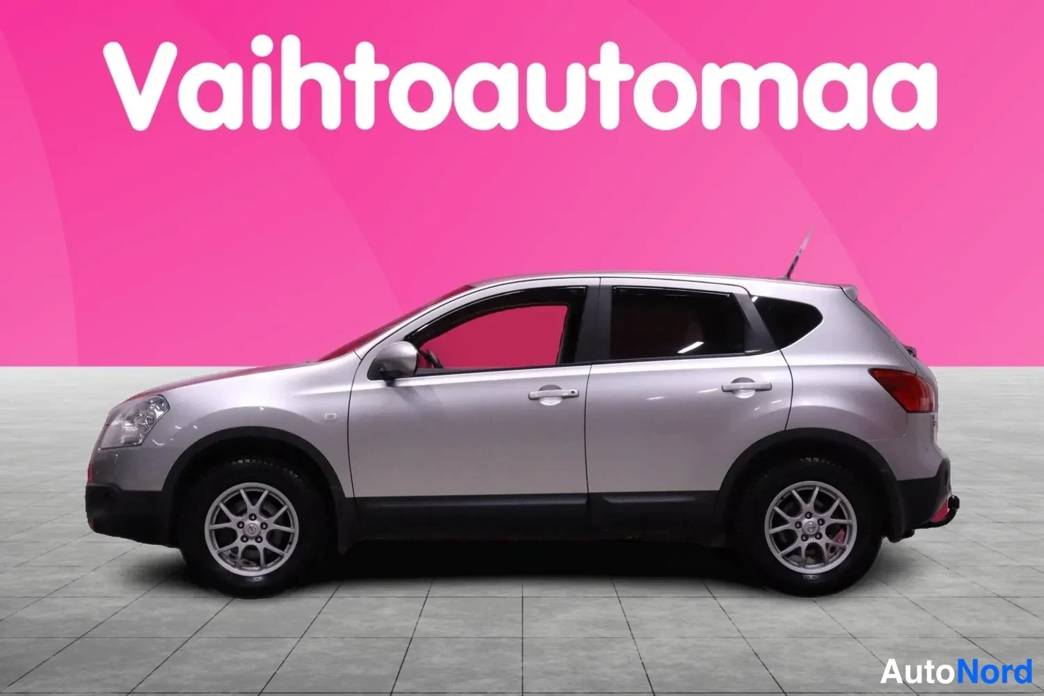 Sivulta: Hopeanharmaa Nissan Qashqai sivulta vasemmalta, kokonainen auto harmaassa lattiaympäristössä.