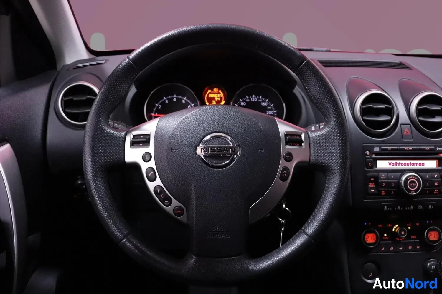 Muu: Nissan-merkitty ohjauspyörä ja kojelaudan mittarit, jotka näyttävat huoltokehotetta, radiopaneeli näkyvissä.