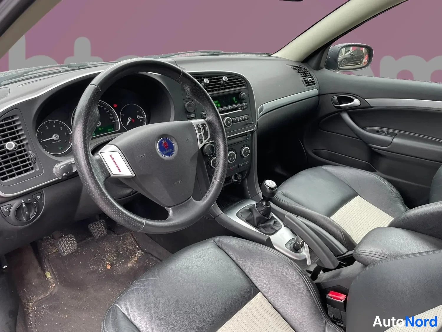 Sivulta: Saab 9-3:n ohjaamo: musta ohjauspyörä, mittaristo, keskikonsoli ja manuaalivaihteisto.