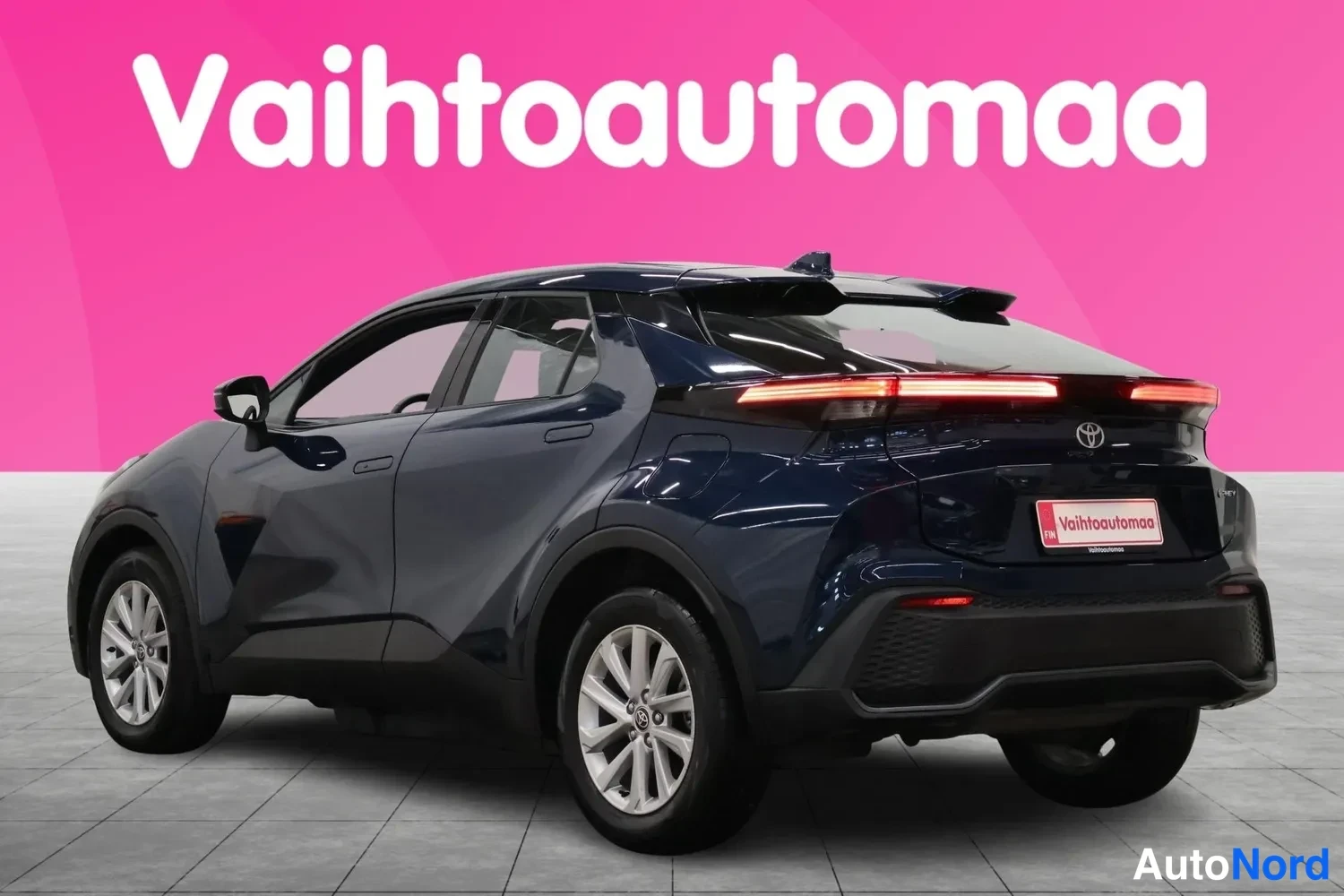 Takaviisto: Sininen Toyota C-HR takaviistosta vasemmalta, takavalot syttyneinä studio-taustalla.