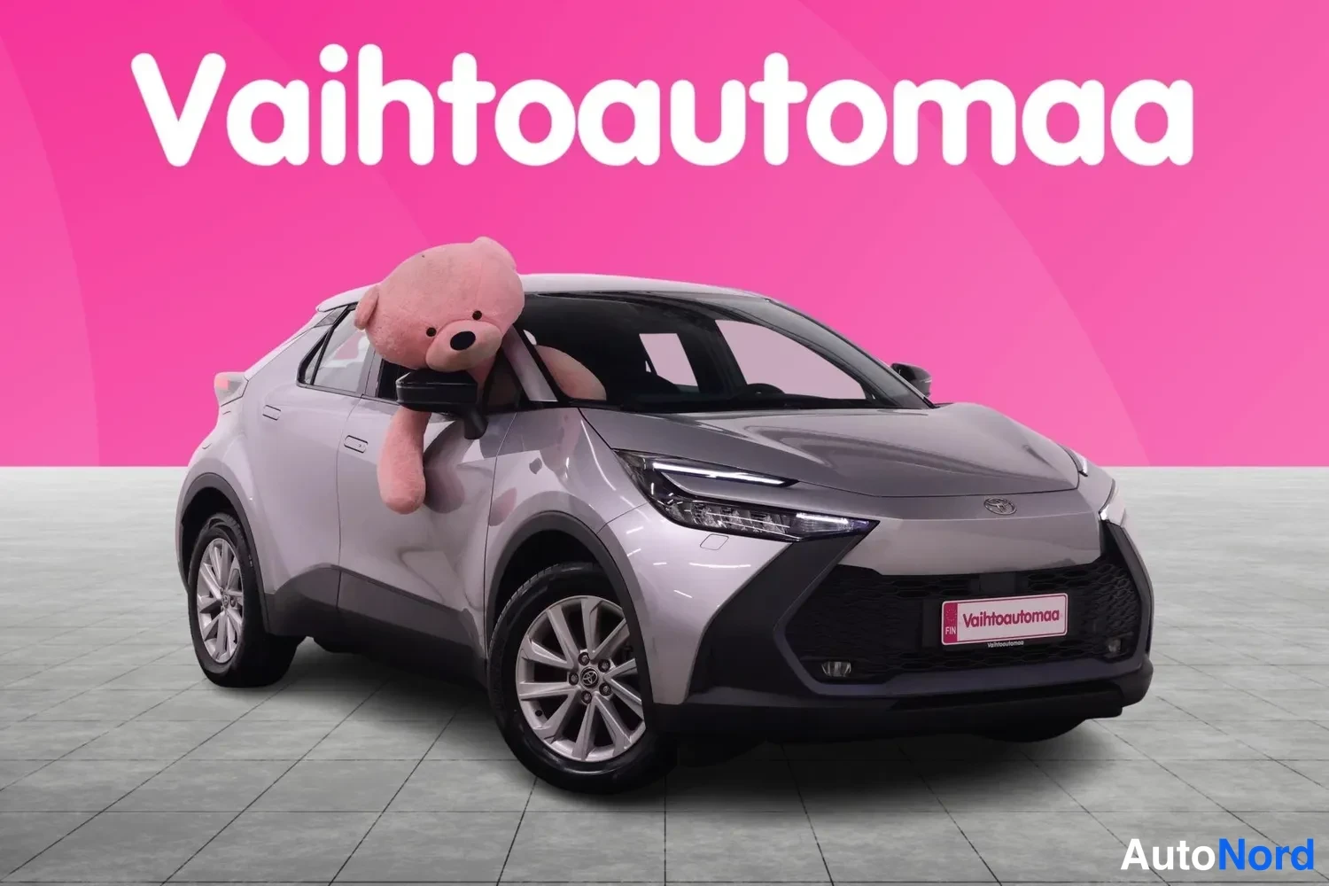 Etuviisto, nokka oikealle: Toyota C-HR etuosaltaan ja sivustaan oikealta kuvattuna, hopeisenpunertavanharmaa koriväri, vaaleat vanteet,markiisinрок tausta.