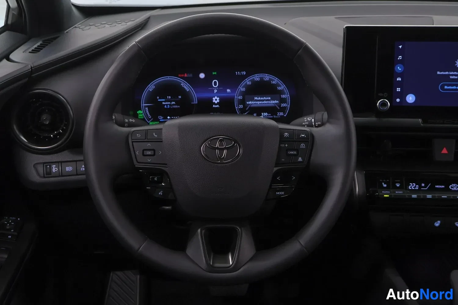 Yksityiskohta: Ohjauspyörä ja mittaristo sisäkuvausta, Toyota-merkki ohjauspyörässä, digitaalinen mittaristo ja infotainment-näyttö.