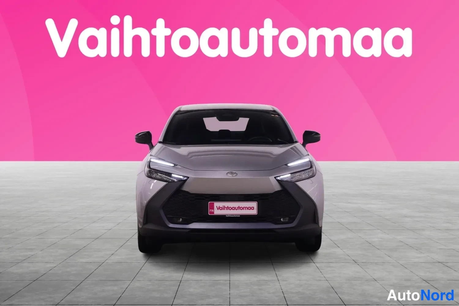 Edestä: Toyota C-HR suoraan edestä kuvattuna, hopeanharmaa koriväri, LED-ajovalot ja tumma etusäleikkö näkyvissä, Vahtoautomaa-kyltti etupuskurissa.