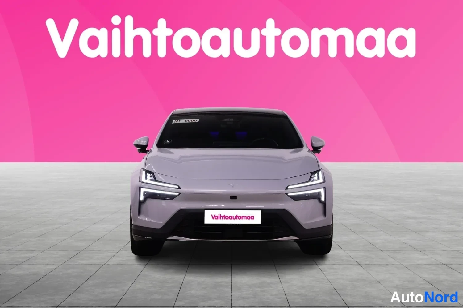 Edestä: Valkoisen Polestar 4:n etunäkymä, tuulilasissa -kilpi ja etupuskurissa Vaihtoautomaa-kyltti.