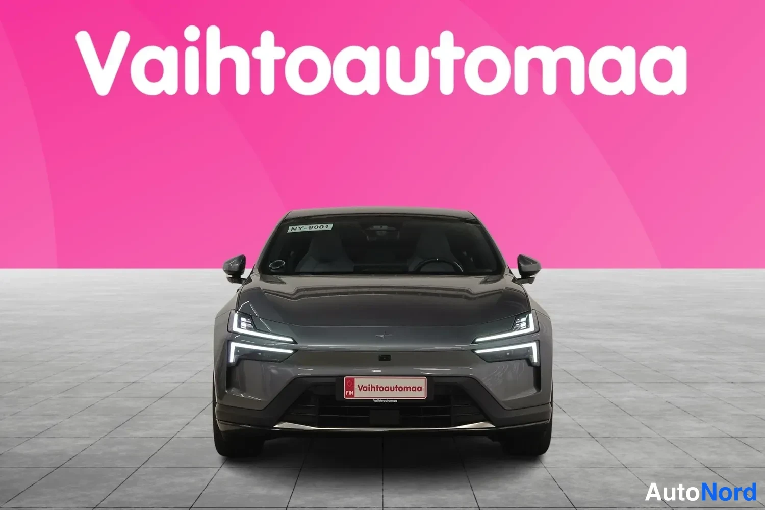 Edestä: Harmaan Polestar 4:n etunäkymä suoraan edestä, LED-ajovalot päällä, rekisterissään Vahtoautomaa-tunnus, pinkki tausta ja Vahtoautomaa-logo.
