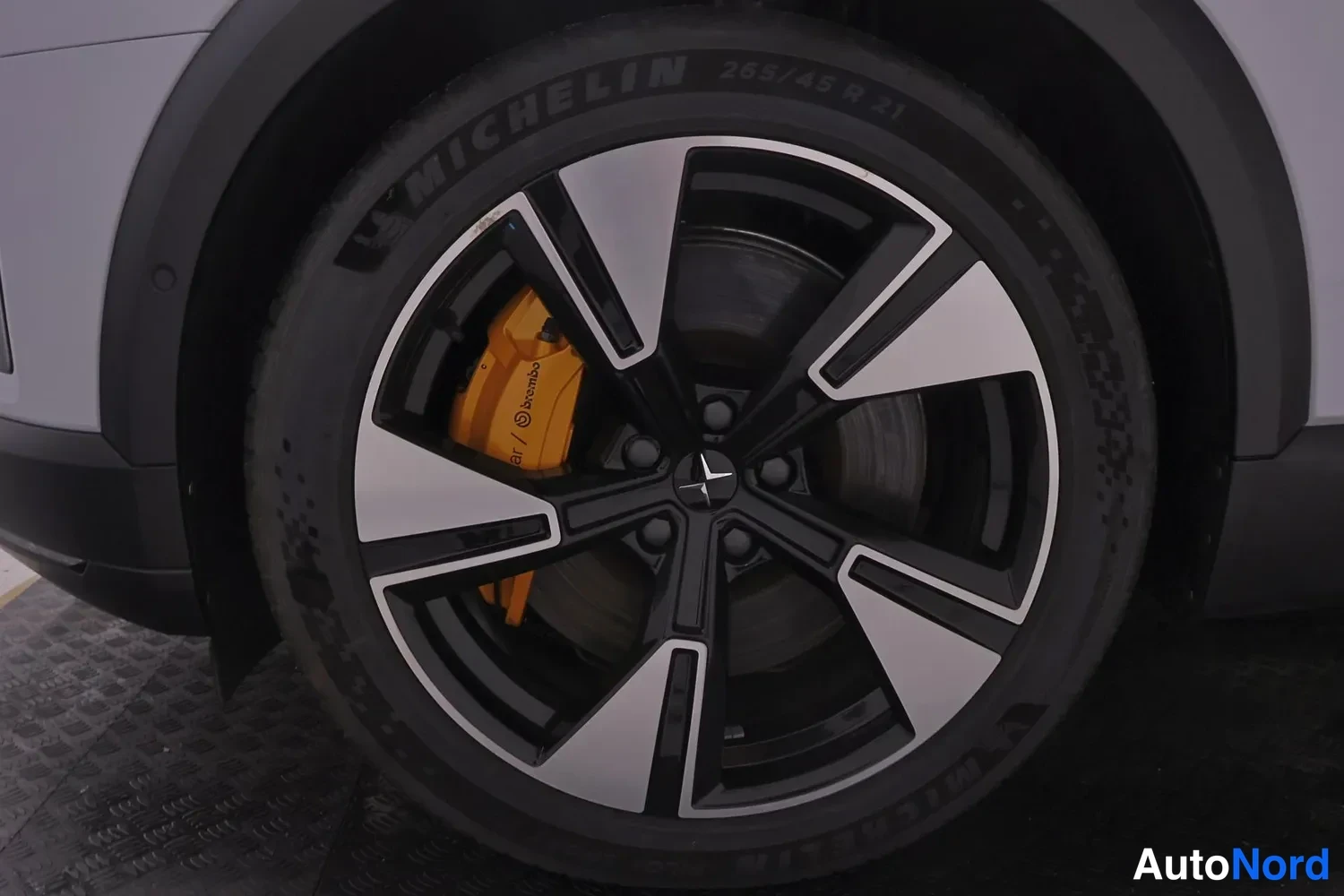 Sivulta: Lähikuva auton pyörästä: hopea-musta kevytmetallivanne, Michelin-rengas 265/45 R 21 ja keltainen Brembo-jarrusatula näkyvät.