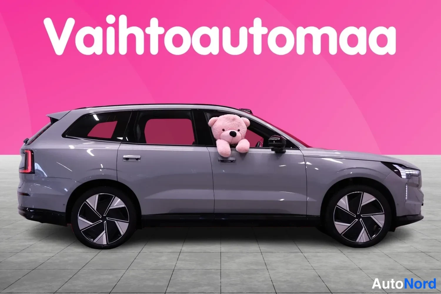 Takaviisto: Volvo EX90:n sivuprofiili vasemmalta vaaleanharmaana, perä- ja etupään kulmat näkyvissä, pinkillä studiosetaalilla