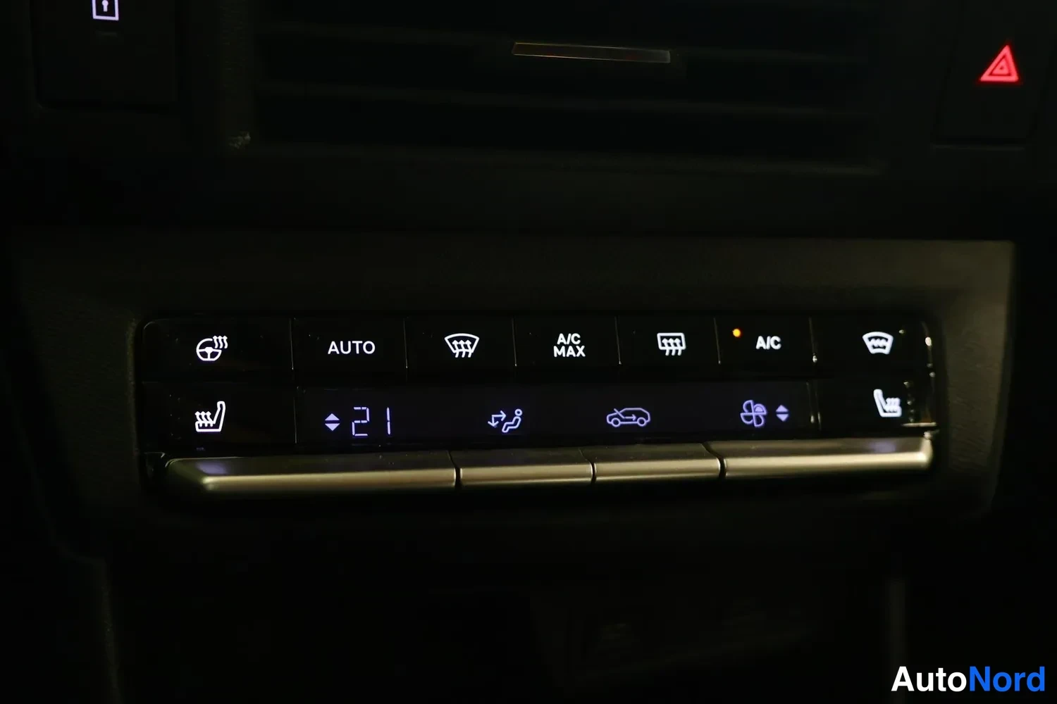 Muu: Ilmastointilaitteen ohjainpaneeli, lämpötila 21 astetta, A/C, A/C MAX ja AUTO-napit sekä istuttimen lämmitys- ja tuuletusmerkit.