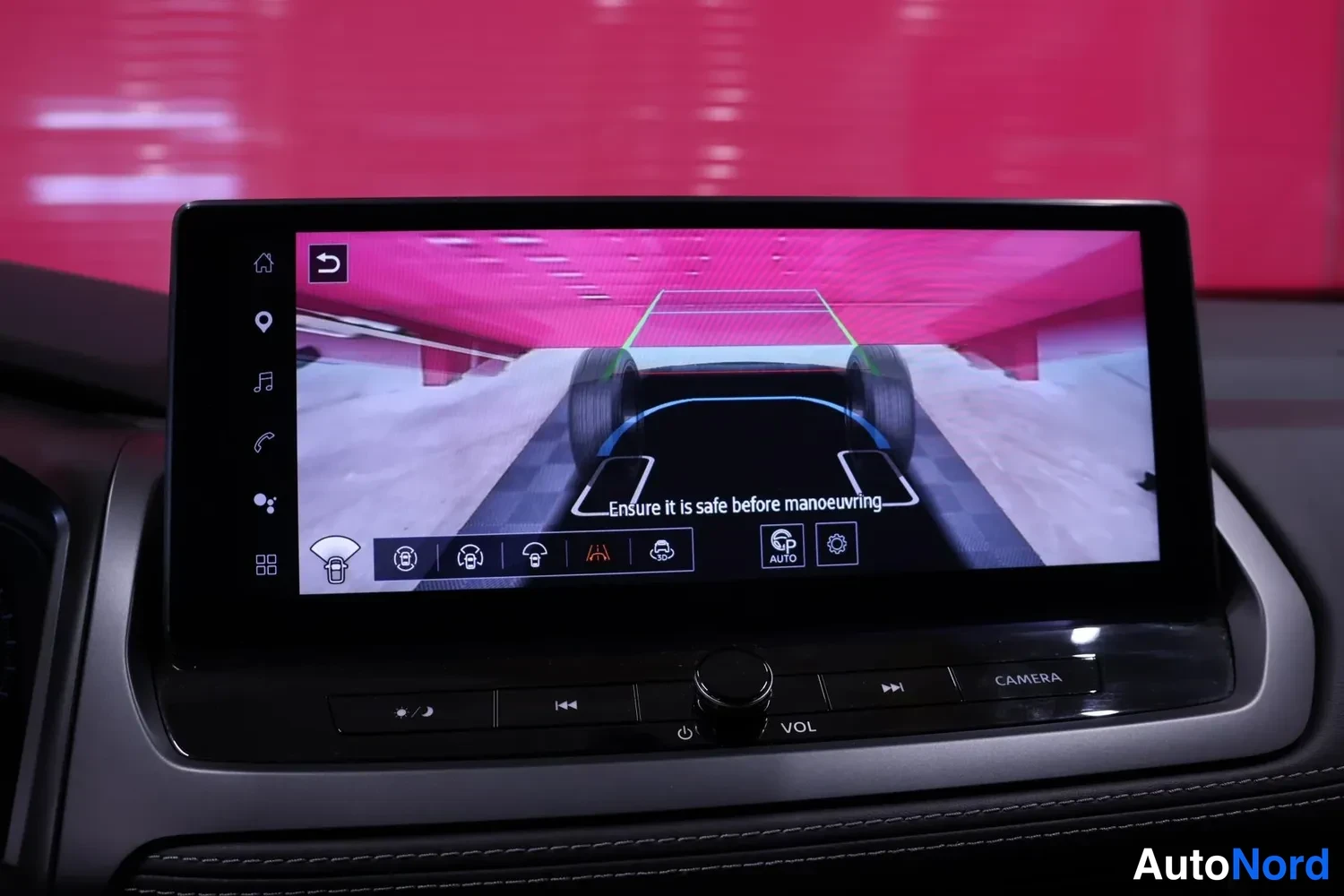 Yksityiskohta: Infotainment-näytöllä pyöränkulma-näkymä, jossa autojen renkaita etualalla ja opastusviivat, teksti 'Ensure it is safe before manoeuvring'.