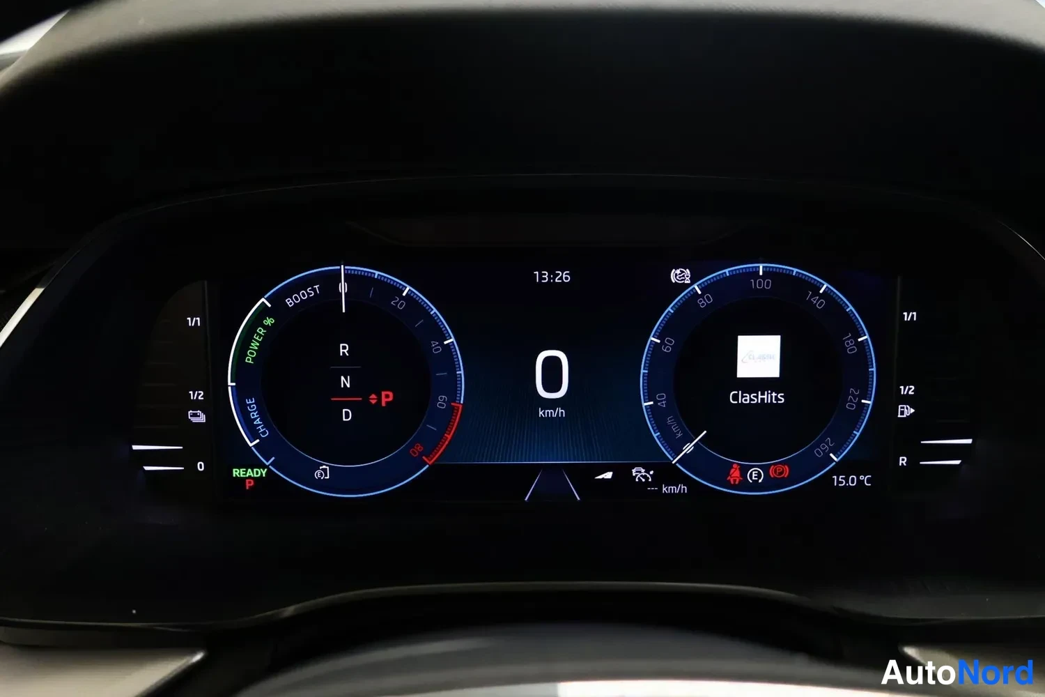 Yksityiskohta: Digitaalinen mittaristo näyttää P-valintatilan, 0 km/h nopeuden, POWER/BOOST/CHARGE-asteikon ja radion soittolistan ClasHits, lämpötila 15,0 °C.