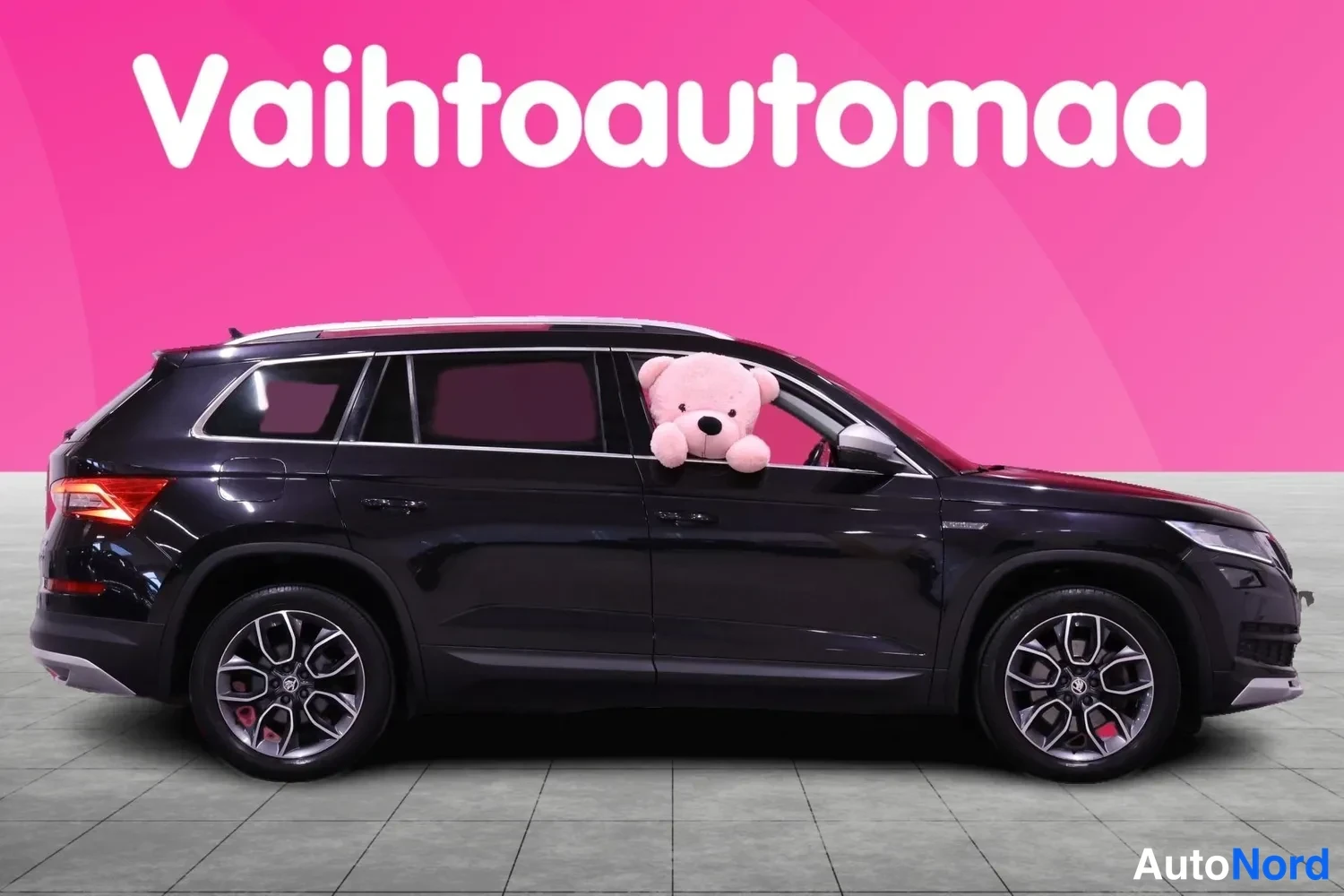 Sivulta: Musta Skoda Kodiaq sivulta oikealta, katolla kattotelineet ja ikkunasta näkyy pehmolelu.