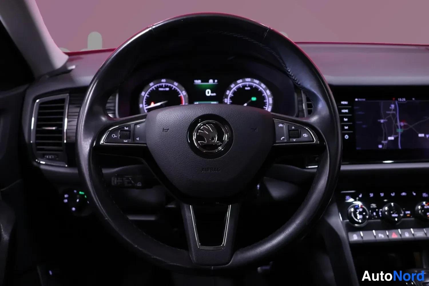 Yksityiskohta: Ohjauspyörä tarkasti esillä: Škoda-merkki keskellä, AIRBAG-teksti, puhelin- ja ääniohjausnapit molemmin puolin, taustalla mittaristo, navigointinäyttö ja kojela