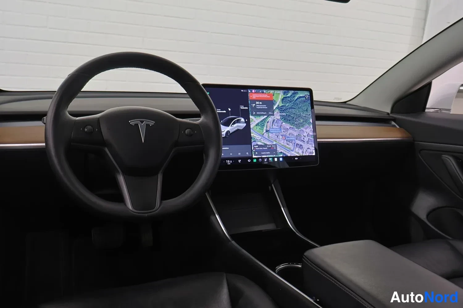 Muu: Ohjaamo kuvattuna kuljettajan paikalta: Tesla-ohjauspyörä ja suuri kosketusnäyttö, jossa navigointikartta.