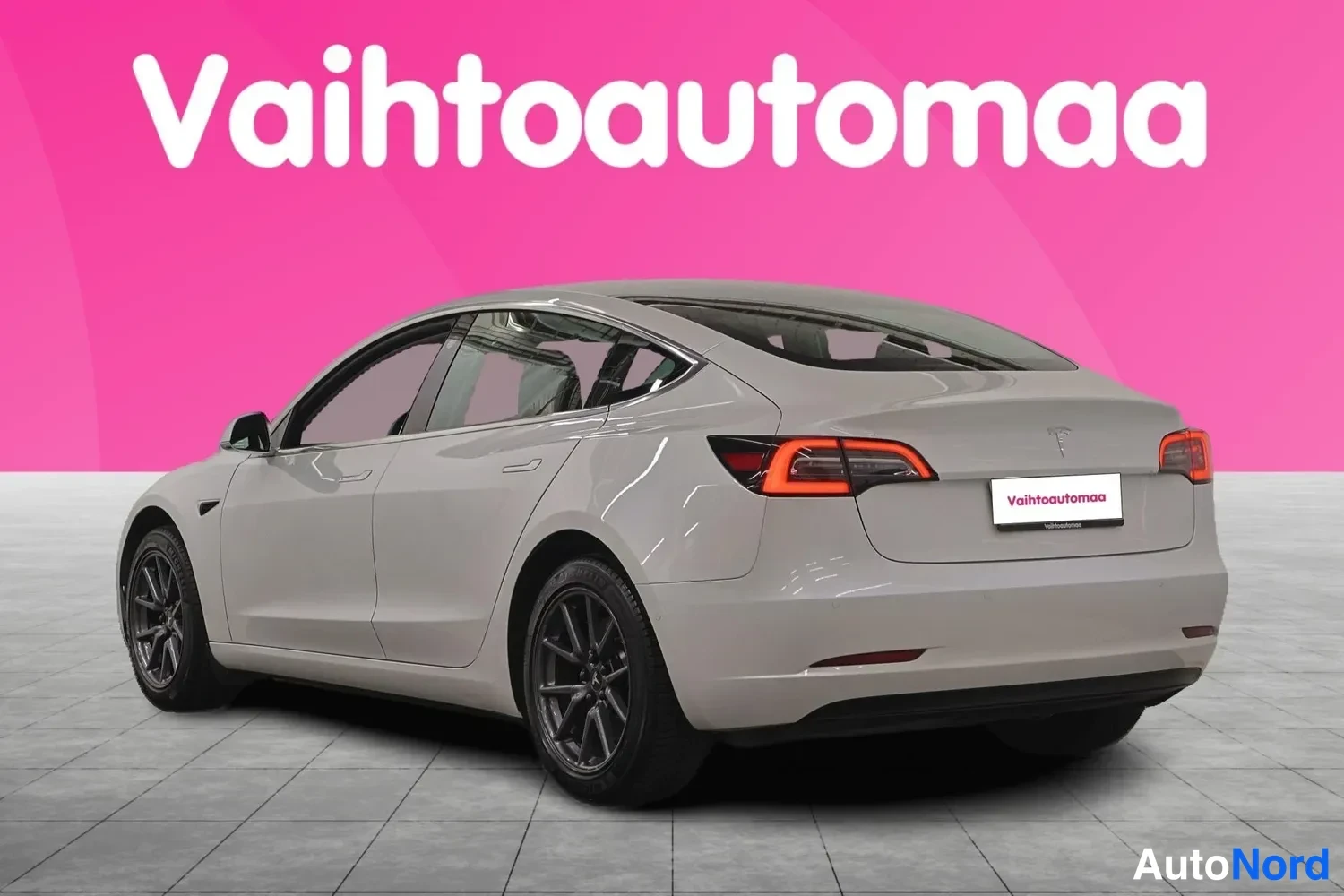 Takaviisto: Tesla Model 3 -auton takanurkkakuva, valkoinen korimalli näkyvissä taustavalokangasta vasten.