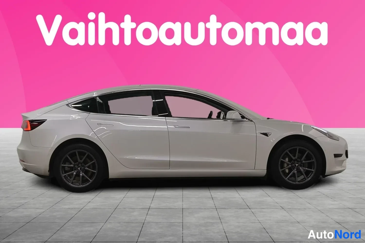 Sivulta: Tesla Model 3:n vasen kylki sivusuunnassa, vaalea pk-vari, tummat vanteet, pinkki tausta.