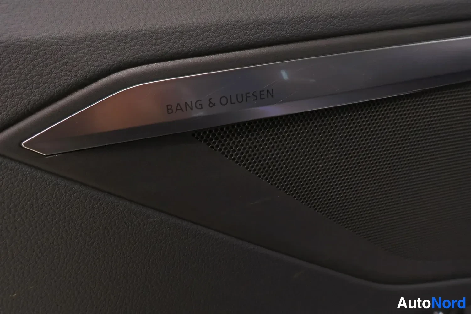 Yksityiskohta: Oven sisäpaneelin detalji: Bang & Olufsen -merkintä kaiuttimen ritilän yläpuolella.