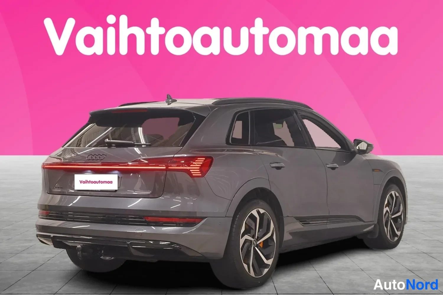 Takaviisto: Audi e-tron S takaa-oikealta kuvattuna, harmaa koriväri, neljä pyöreää pakoputkia muistuttavaa korostetta ja vetokoukku näkyvissä.