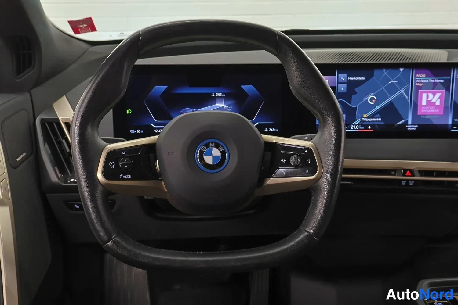 Etuviisto: Ohjauspöytä ja monivälkytinnäyttö: BMW-ohjauspyörä ja laaja näyttö, jossa navigointikartta ja mediavalikko.